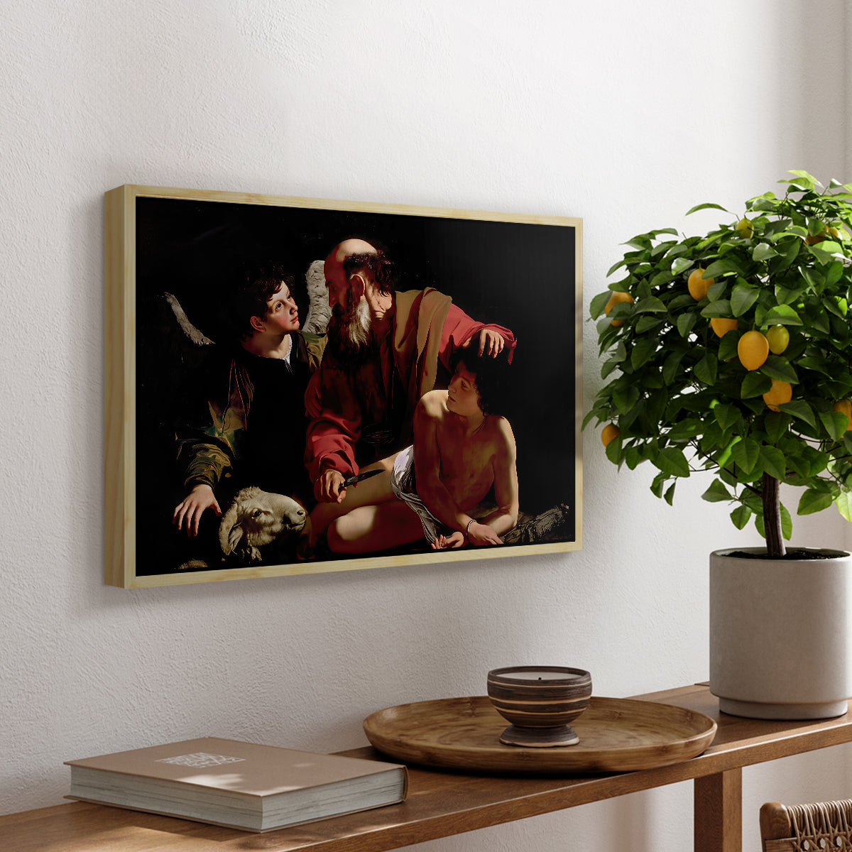 The Sacrifice of Isaac (Uffizi Version), c. 1603 by Caravaggio, presented in a natural wood floater framed canvas featuring Abraham holding Isaac while angel intervenes to stop the sacrifice, displayed above a hallway console table.
