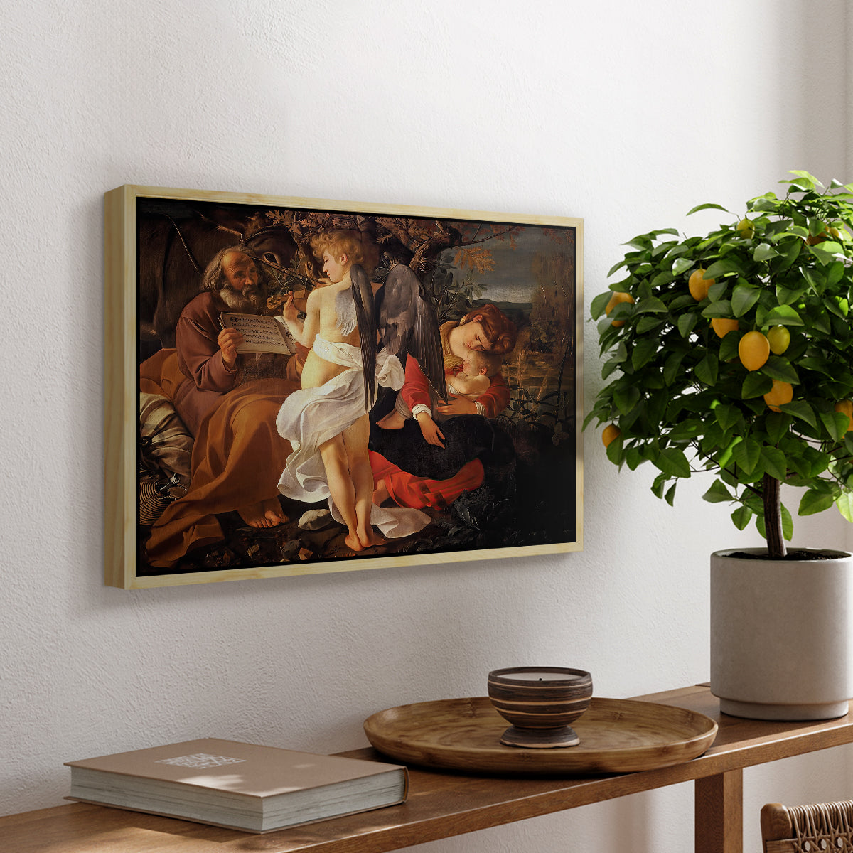 Rest on the Flight into Egypt, c. 1597 by Caravaggio, presented in a natural wood floater framed canvas featuring the Holy Family resting in landscape with angel playing violin, displayed above a hallway console table.