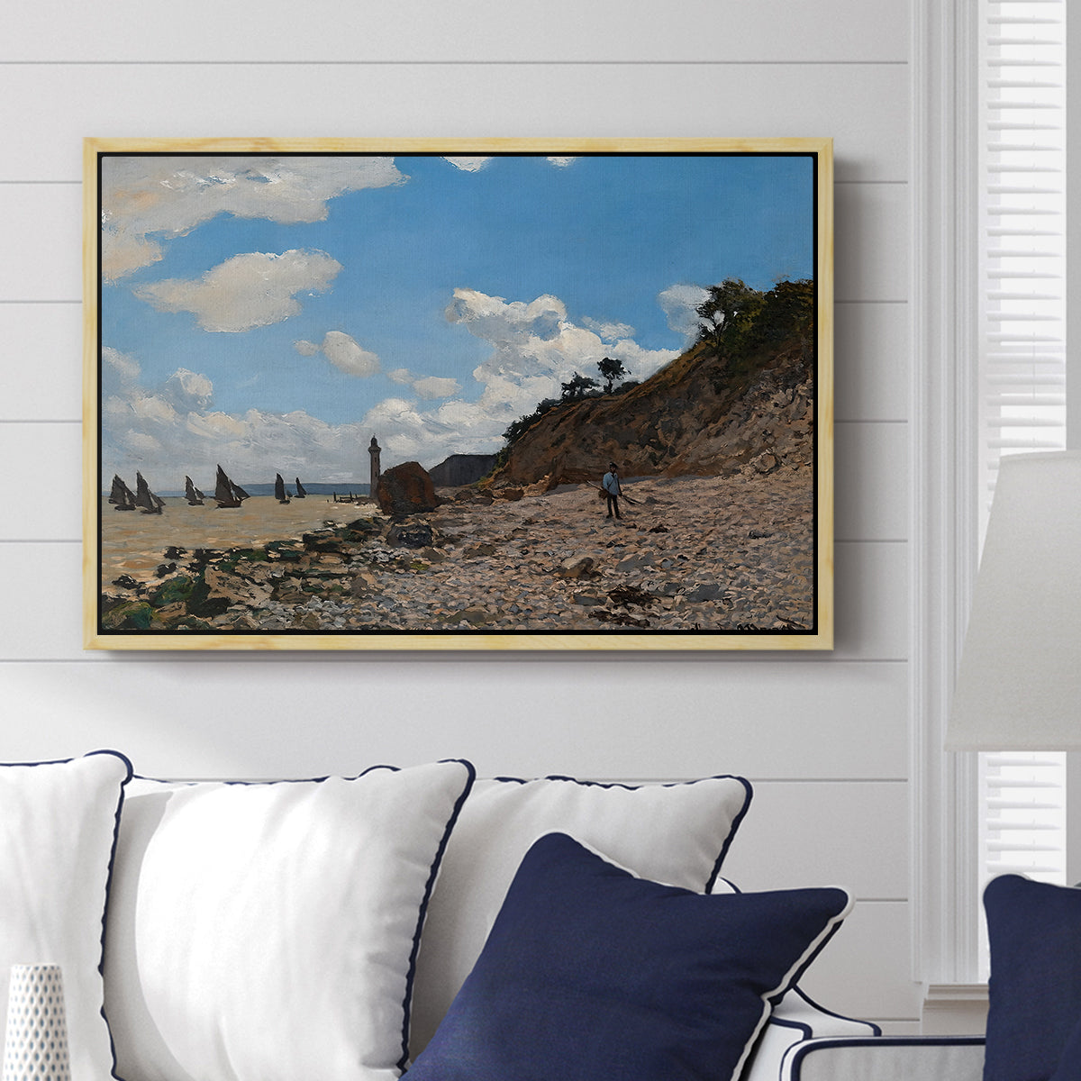 The Beach at Honfleur, 1864 by Claude Monet displayed above a sofa in a living room in a natural wood floater frame, featuring an impressionist seaside with people and sailboats under bright sky.
