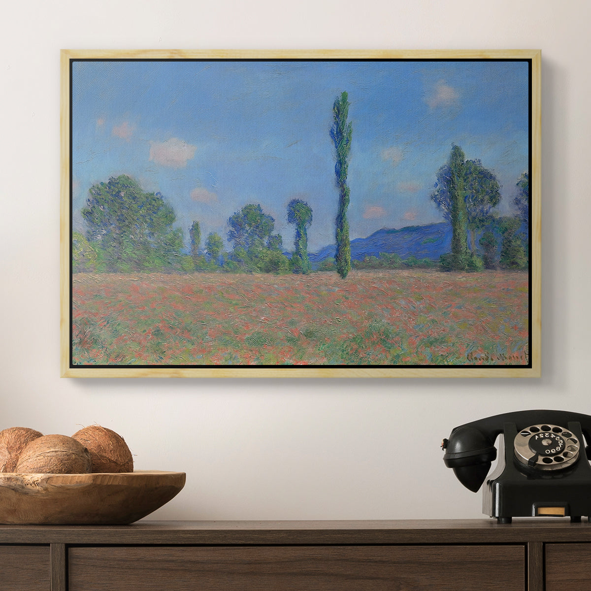 Poppy Field (Giverny), 1890-1891 by Claude Monet in a natural wood floater framed canvas displayed above a console table in a hallway, featuring a rural field filled with red blossoms beneath open sky.