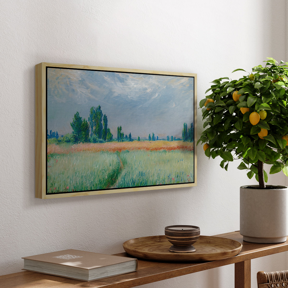 The Wheat Field (Champ de Blé), 1881 by Claude Monet, presented in a natural wood floater framed canvas featuring a golden wheat field stretching across landscape under soft sky, displayed above a hallway console table.
