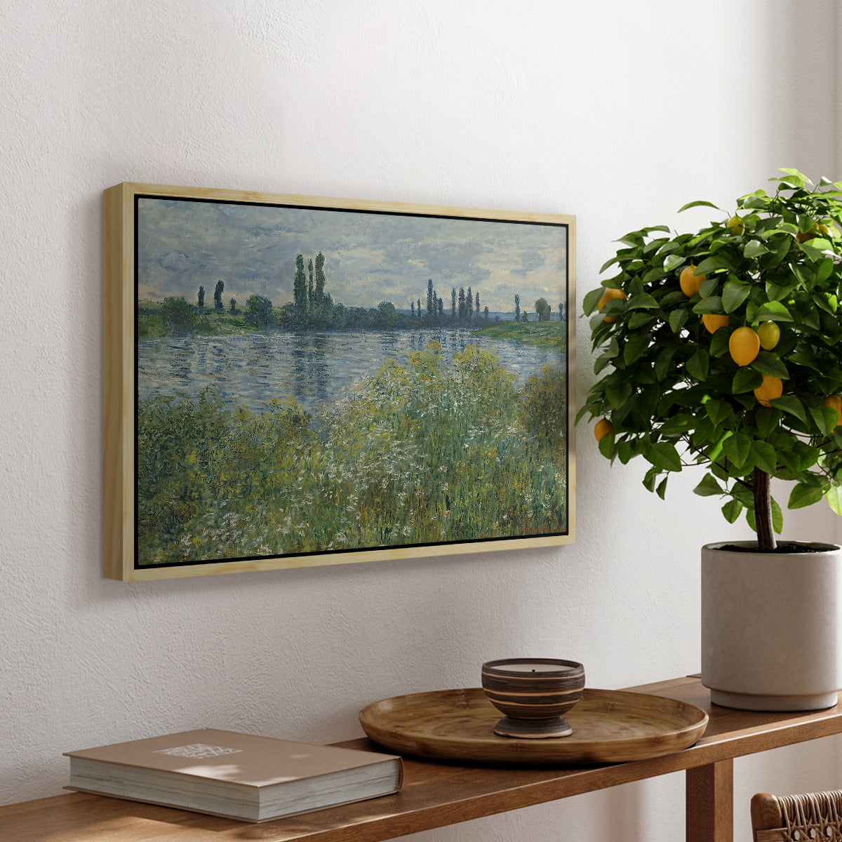 Banks of the Seine, Vétheuil, 1880 by Claude Monet, presented in a natural wood floater framed canvas featuring a riverbank landscape with water, trees, and distant village buildings, displayed above a hallway console table.
