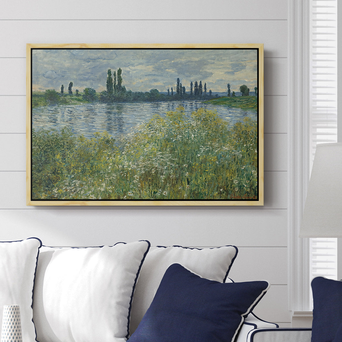 Banks of the Seine, Vétheuil, 1880 by Claude Monet displayed above a sofa in a living room in a natural wood floater frame, featuring an impressionist view of Seine with reflections and greenery.