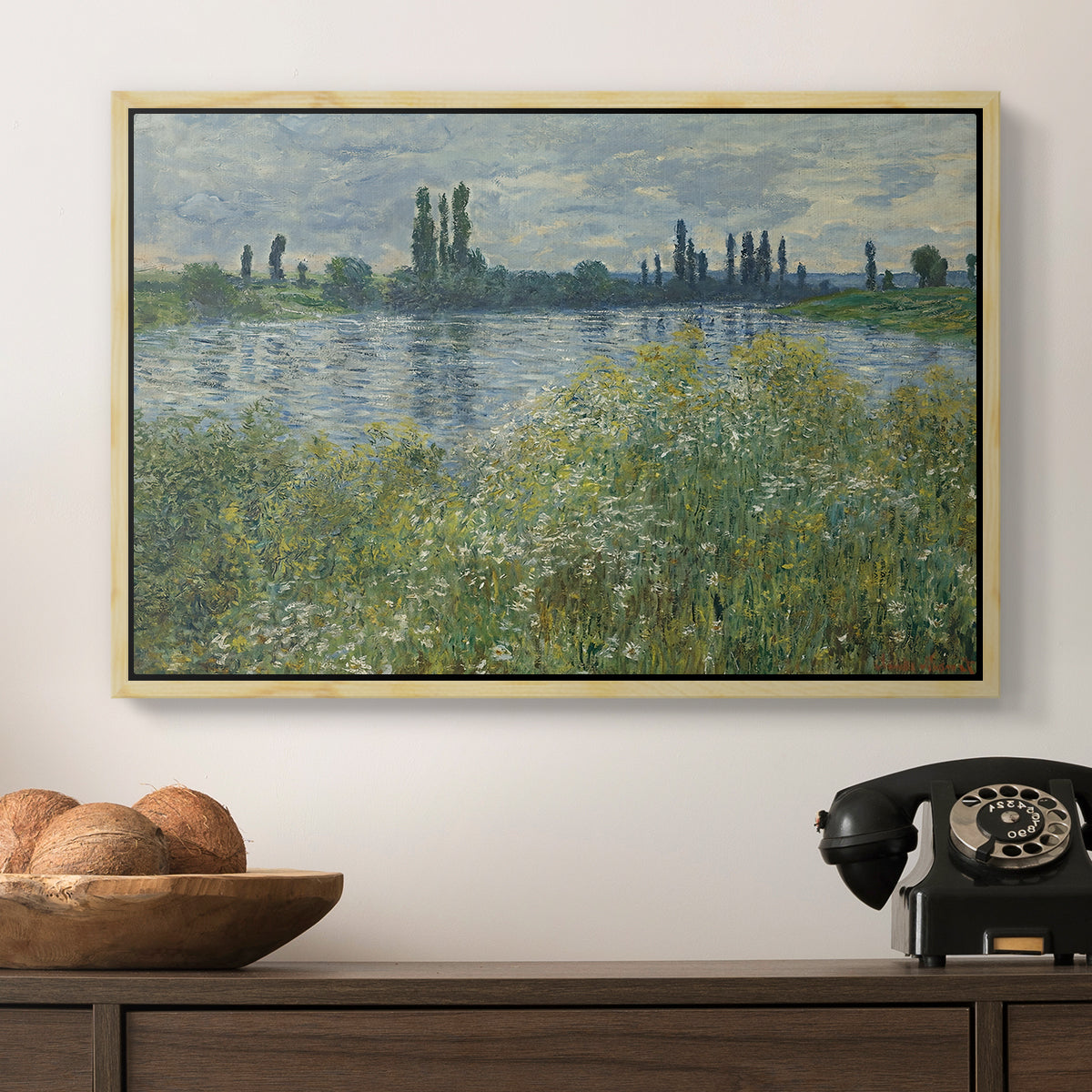 Banks of the Seine, Vétheuil, 1880 by Claude Monet in a natural wood floater framed canvas displayed above a console table in a hallway, featuring a natural landscape with calm water and soft foliage.