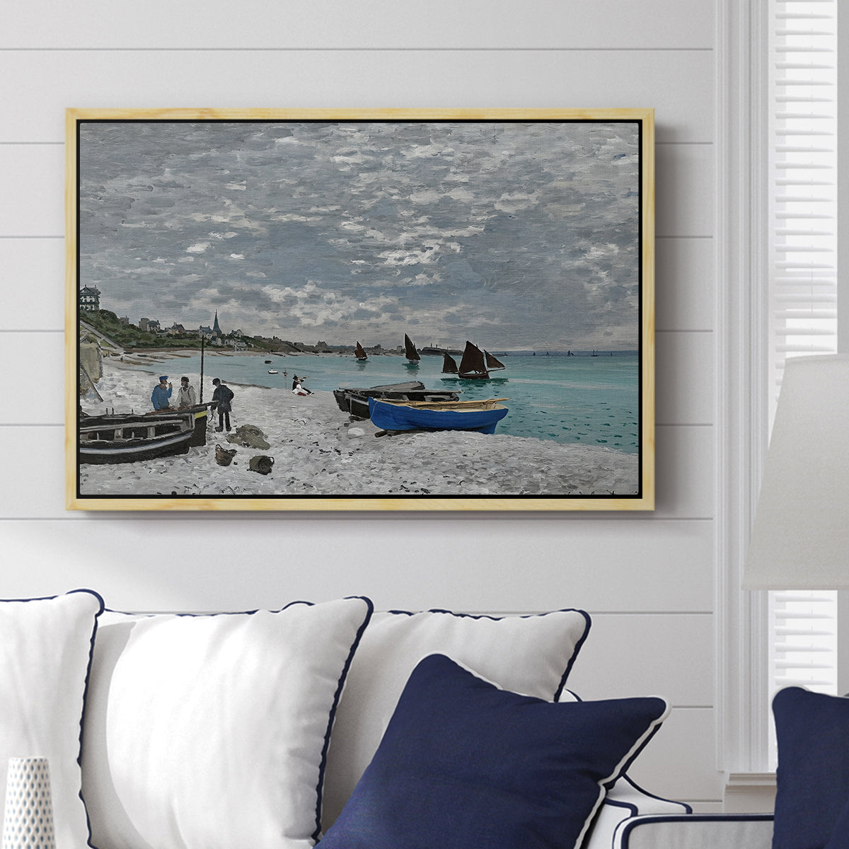 The Beach at Sainte-Adresse, 1867 by Claude Monet displayed above a sofa in a living room in a natural wood floater frame, featuring a lively beach scene with people overlooking water and ships.
