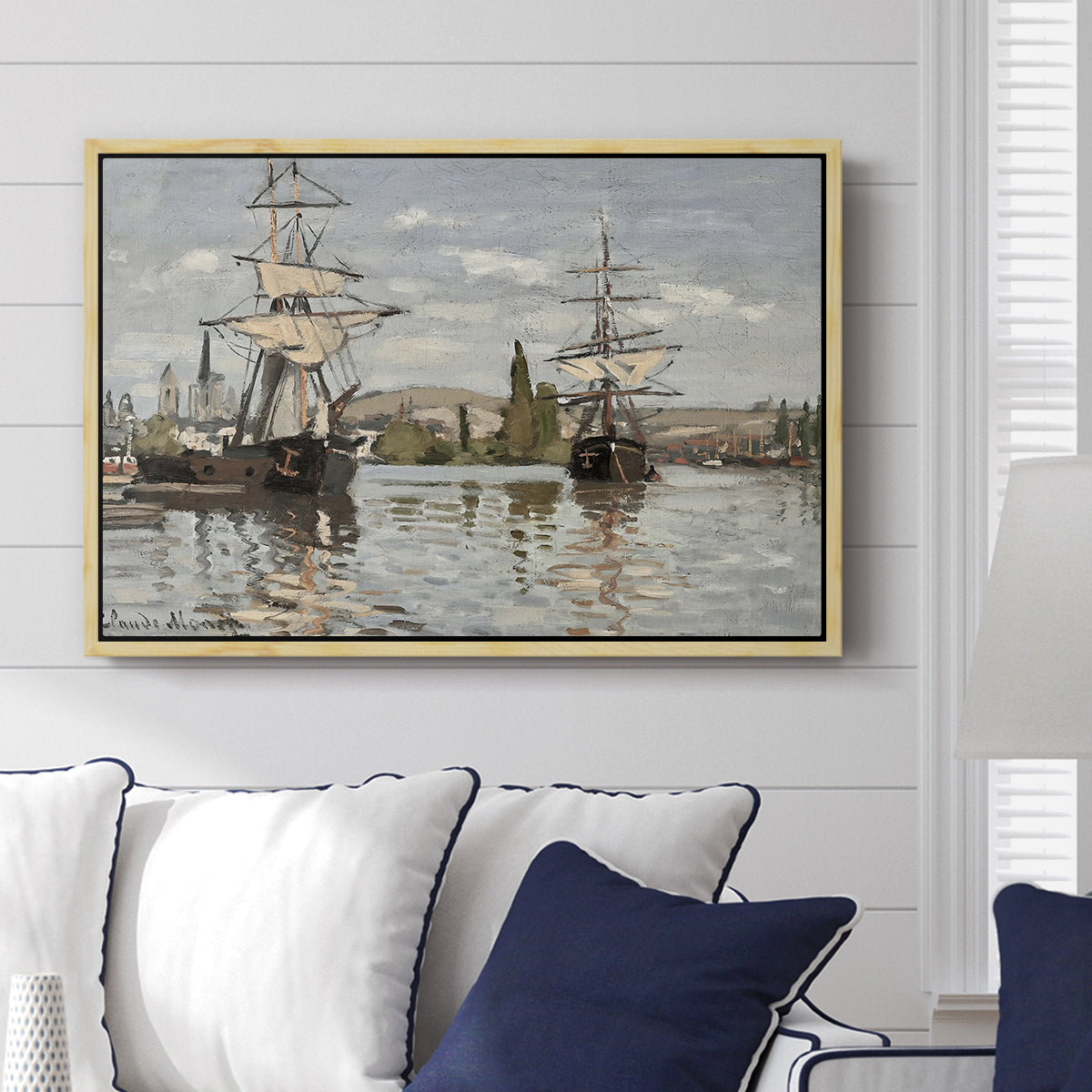 Ships Riding on the Seine at Rouen, 1872 by Claude Monet displayed above a sofa in a living room in a natural wood floater frame, featuring an impressionist river scene with anchored sailing ships and reflections.