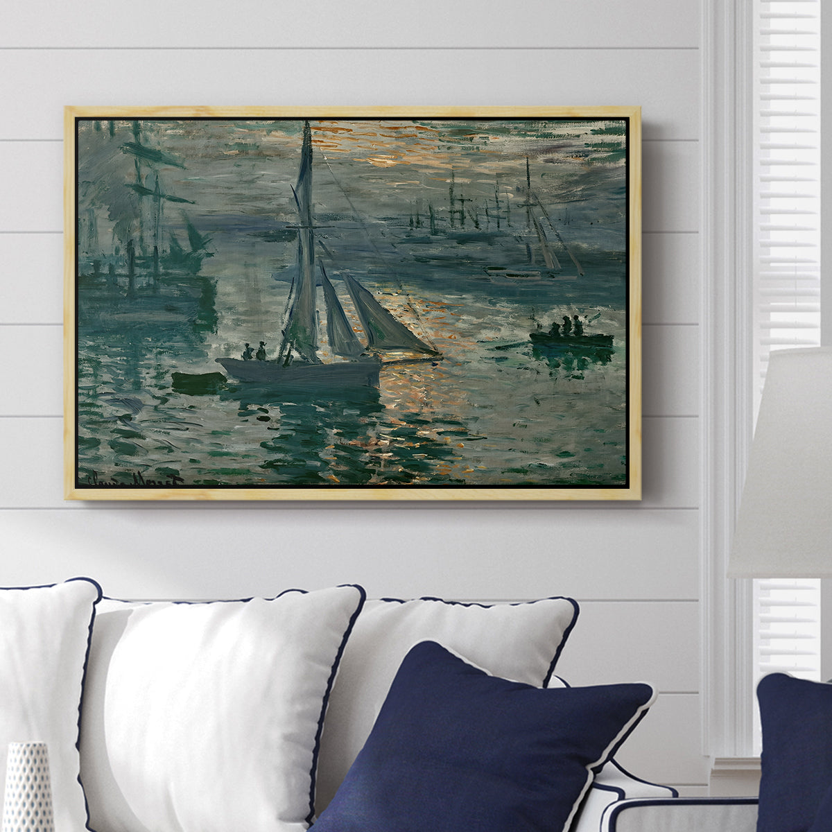 Sunrise (Marine), 1873 by Claude Monet displayed above a sofa in a living room in a natural wood floater frame, featuring an impressionist seascape with glowing sun and misty water.