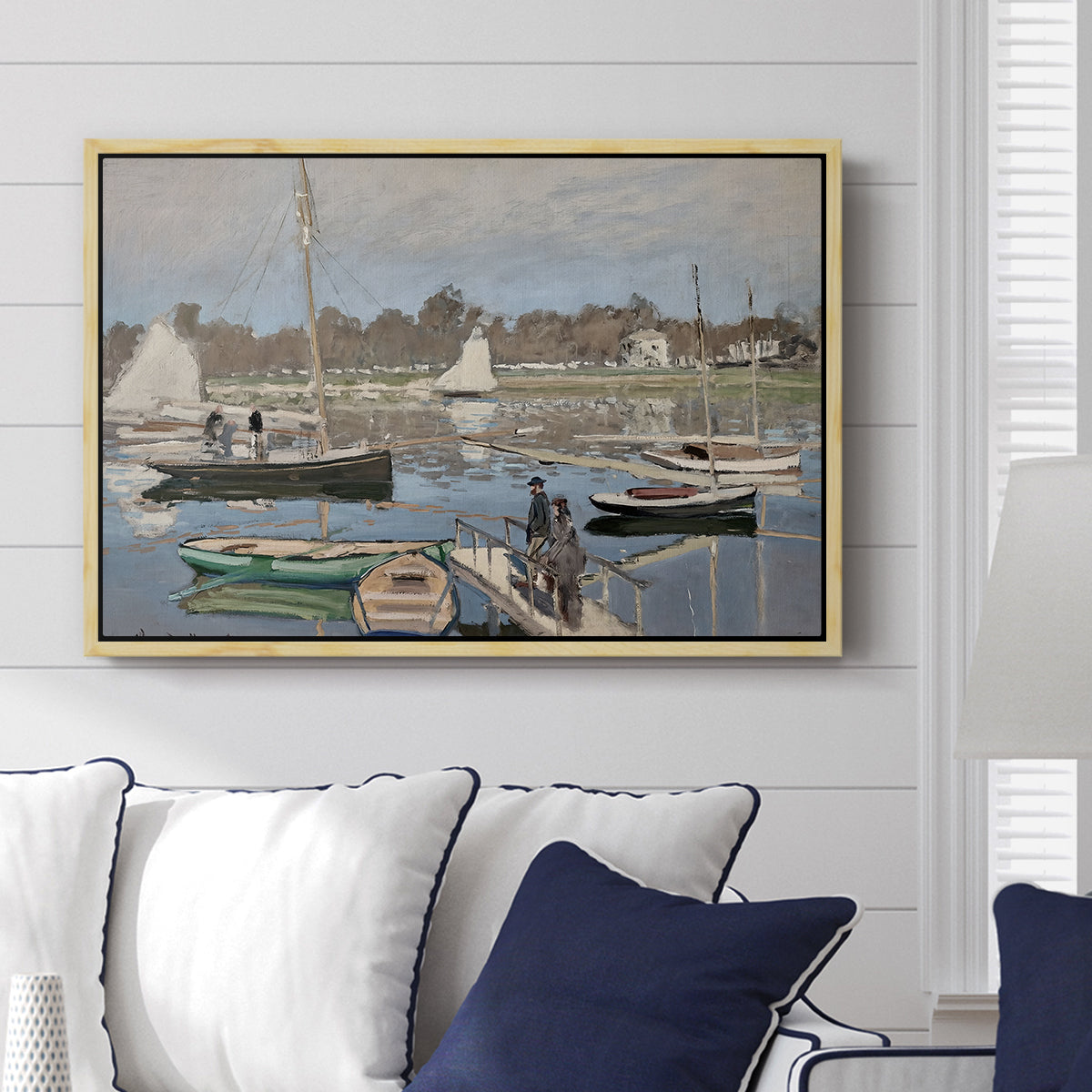 The Basin at Argenteuil, 1874 by Claude Monet displayed above a sofa in a living room in a natural wood floater frame, featuring an impressionist boating scene with clustered masts and gentle ripples.