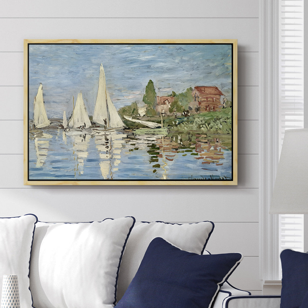 Regatta at Argenteuil, 1872 by Claude Monet displayed above a sofa in a living room in a natural wood floater frame, featuring a lively regatta scene with multiple boats and fluttering sails.