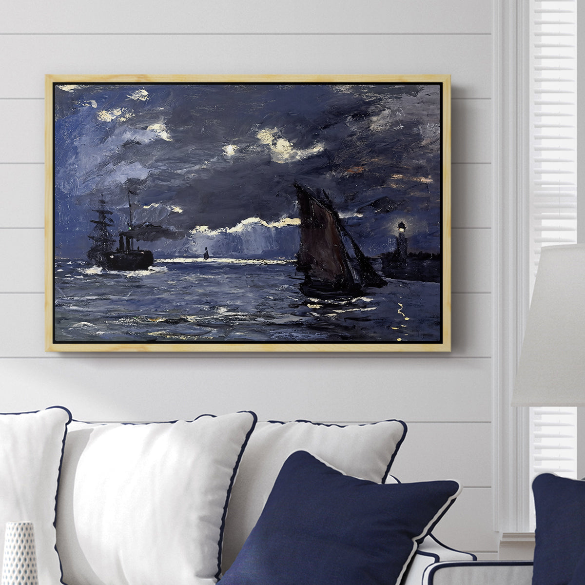 A Seascape, Shipping by Moonlight, 1864 by Claude Monet displayed above a sofa in a living room in a natural wood floater frame, featuring a nocturnal seascape with boats silhouetted against glowing moon.