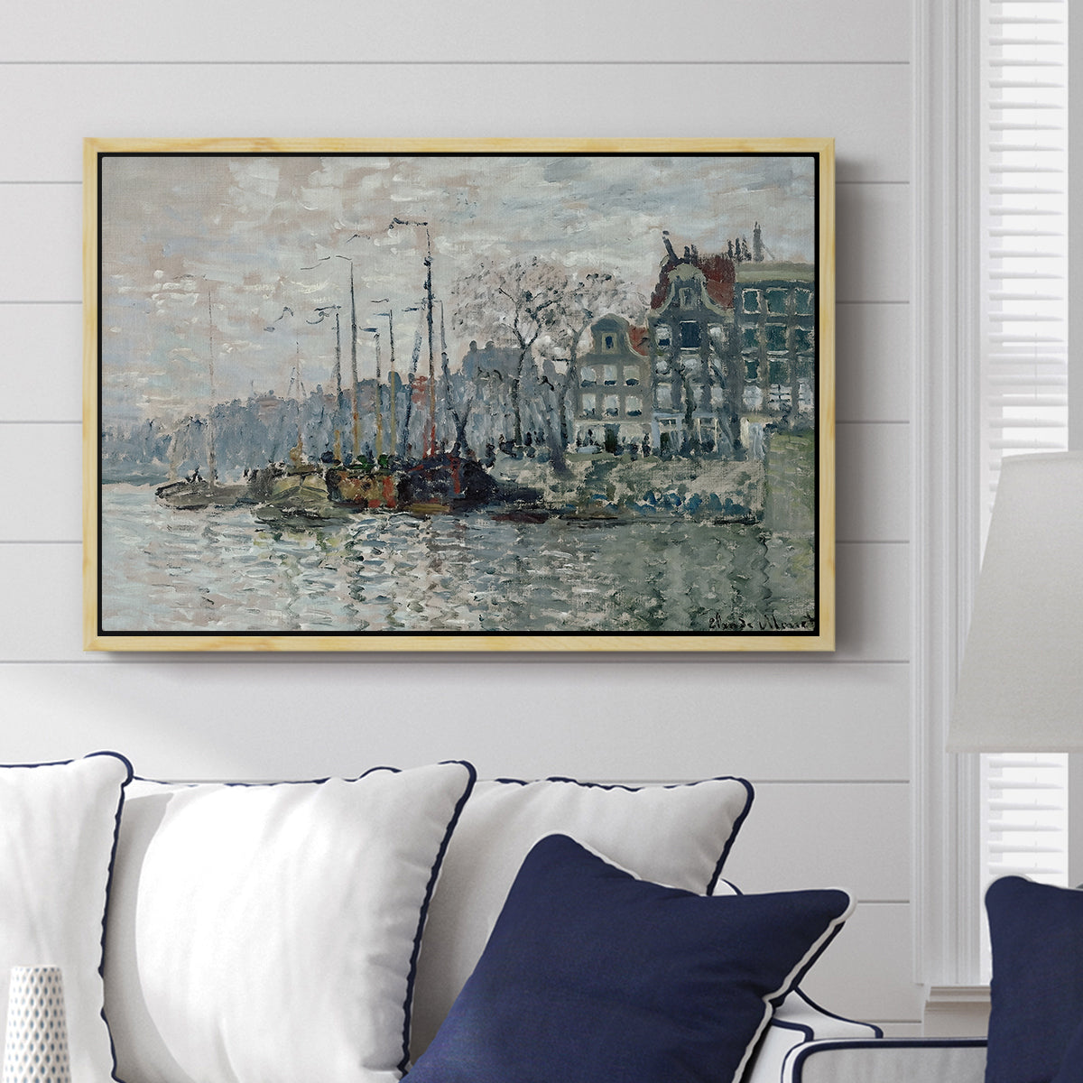 View of the Prins Hendrikkade and Kromme Waal in Amsterdam, 1874 by Claude Monet displayed above a sofa in a living room in a natural wood floater frame, featuring an impressionist cityscape of canal with ships and architecture.