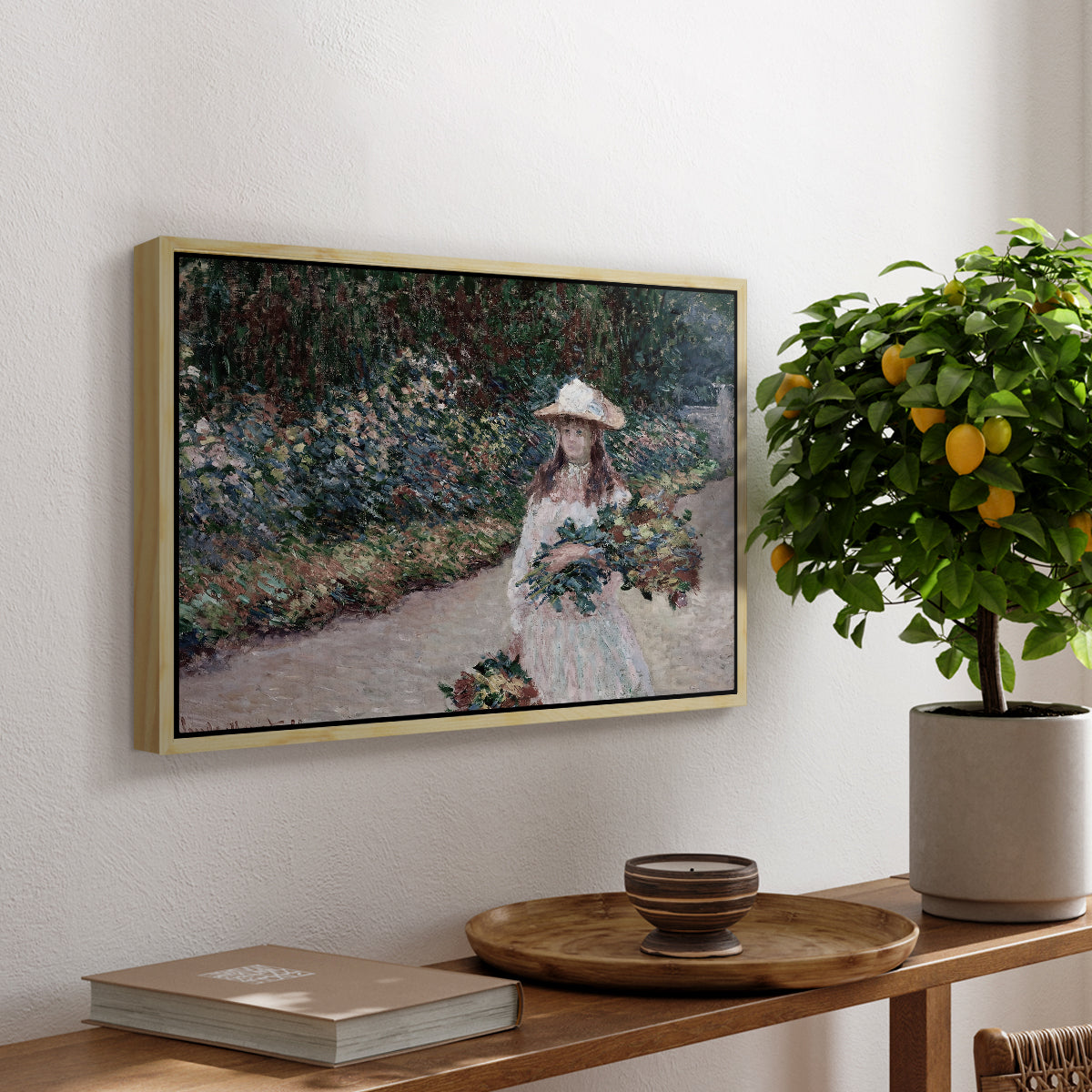Young Girl in the Garden at Giverny, 1888 by Claude Monet, presented in a natural wood floater framed canvas featuring a young girl seated in lush garden surrounded by blooming flowers, displayed above a hallway console table.