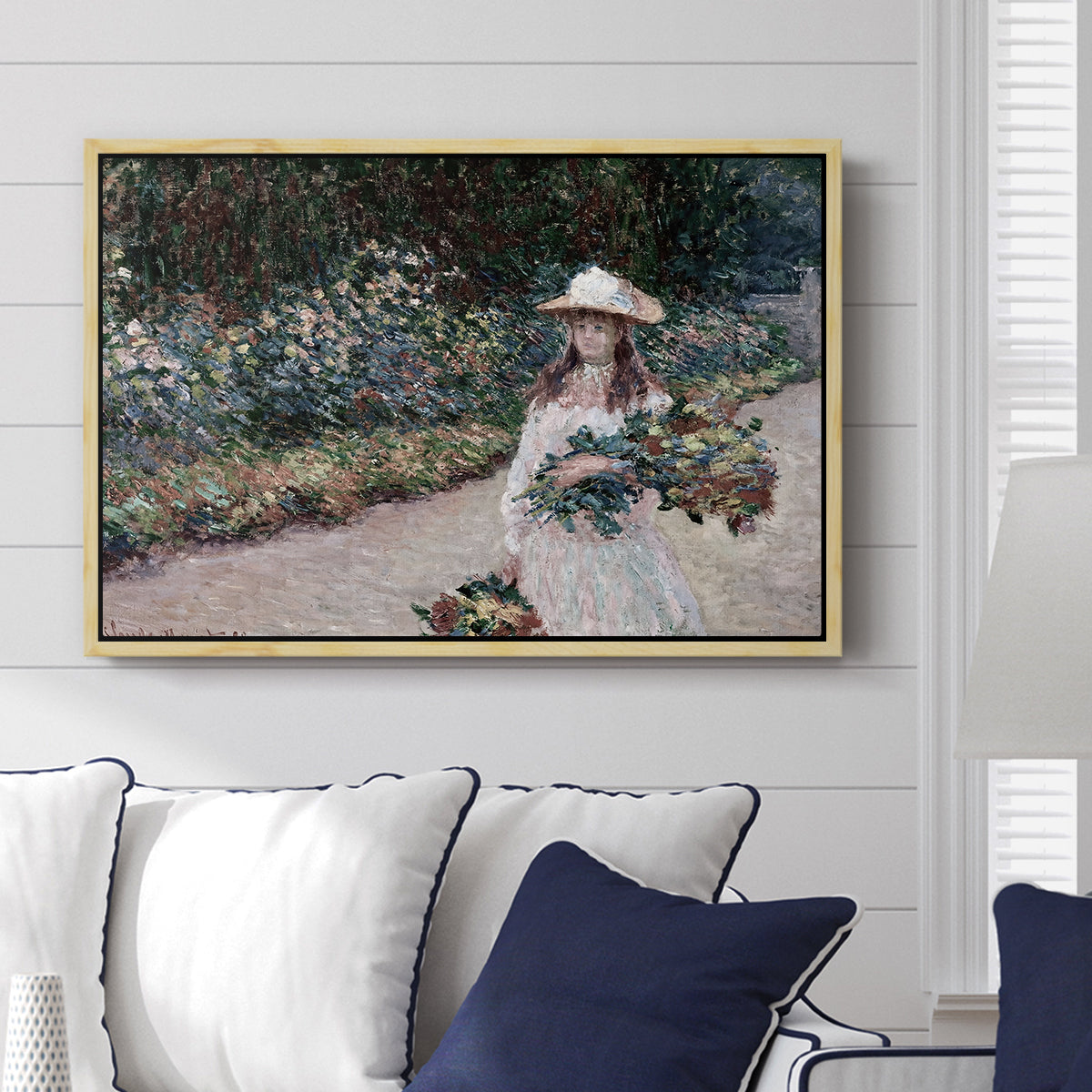 Young Girl in the Garden at Giverny, 1888 by Claude Monet displayed above a sofa in a living room in a natural wood floater frame, featuring an impressionist garden scene with child among greenery and blossoms.