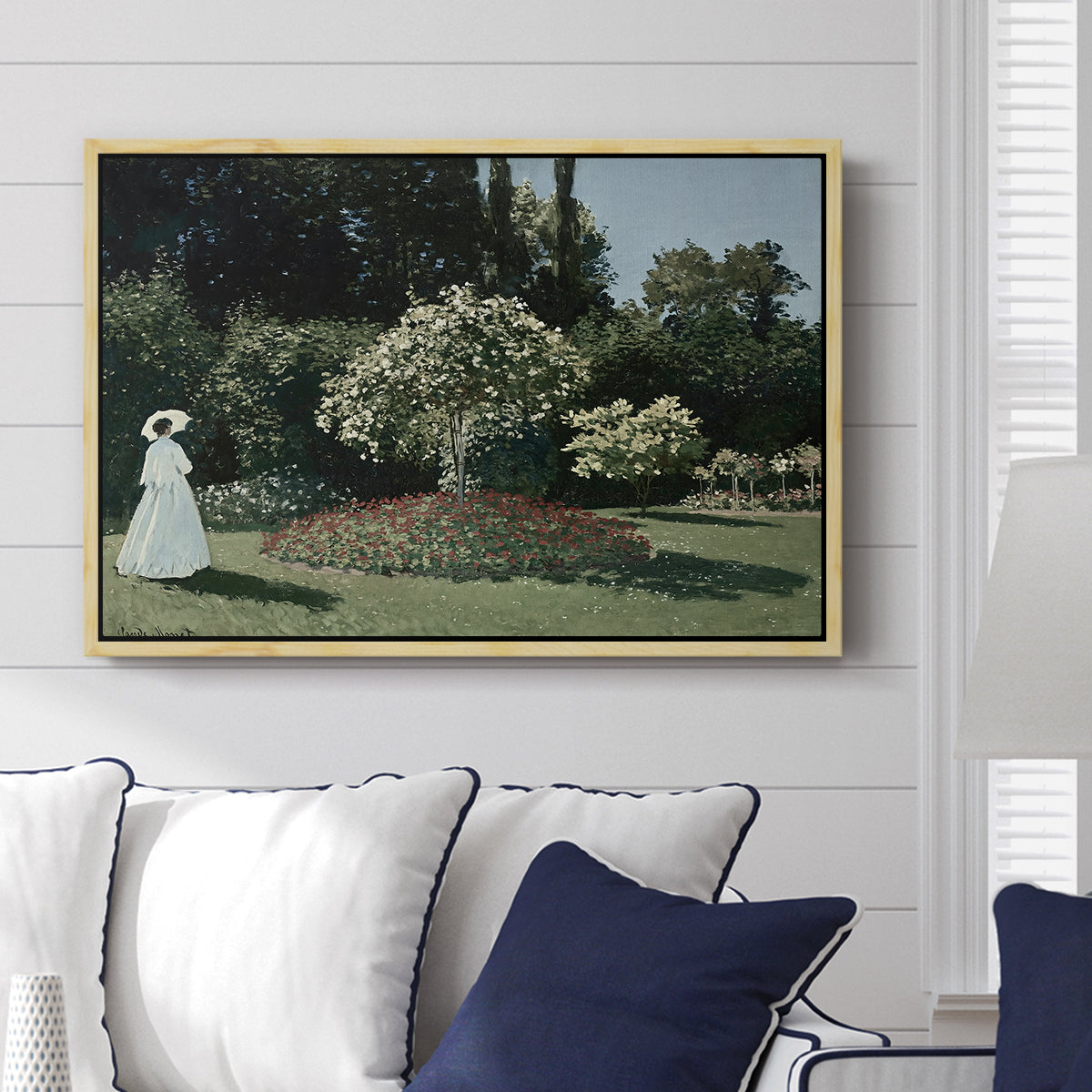 Woman in the Garden, Sainte-Adresse, 1867 by Claude Monet displayed above a sofa in a living room in a natural wood floater frame, featuring an impressionist figure in sunlit garden with lush vegetation.