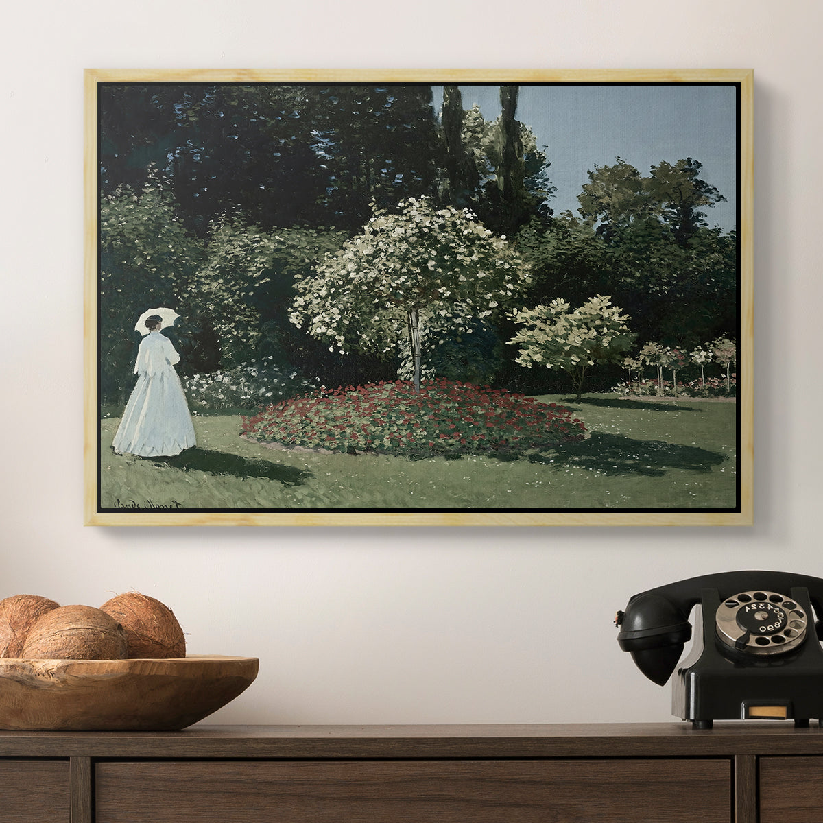 Woman in the Garden, Sainte-Adresse, 1867 by Claude Monet in a natural wood floater framed canvas displayed above a console table in a hallway, featuring a tranquil garden portrait with soft natural light.