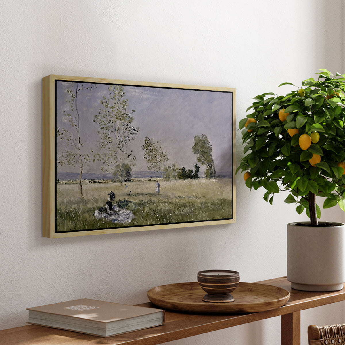 Summer (L'ete), 1874 by Claude Monet, presented in a natural wood floater framed canvas featuring a woman seated in grassy field beneath tree in bright summer landscape, displayed above a hallway console table.