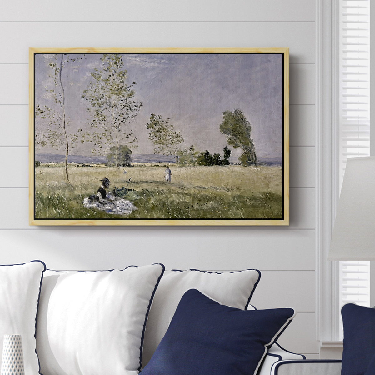 Summer (L'ete), 1874 by Claude Monet displayed above a sofa in a living room in a natural wood floater frame, featuring an impressionist countryside scene with figure resting in shade.