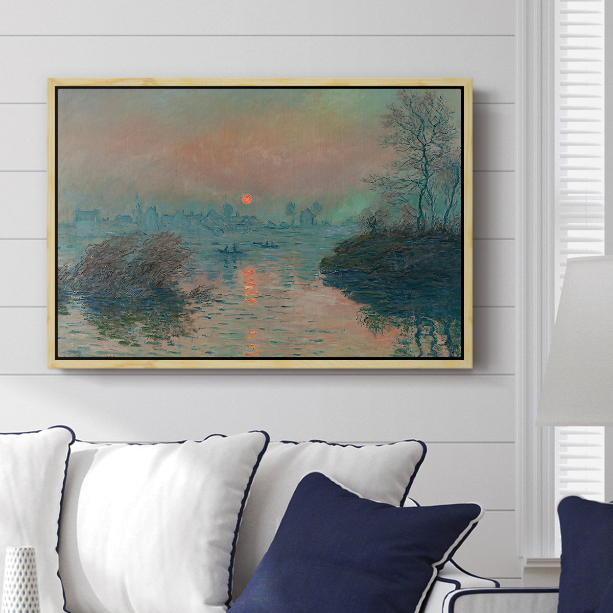 Sunset on the Seine at Lavacourt, Winter Effect, 1880 by Claude Monet displayed above a sofa in a living room in a natural wood floater frame, featuring a winter scene with warm light reflecting on water at dusk.