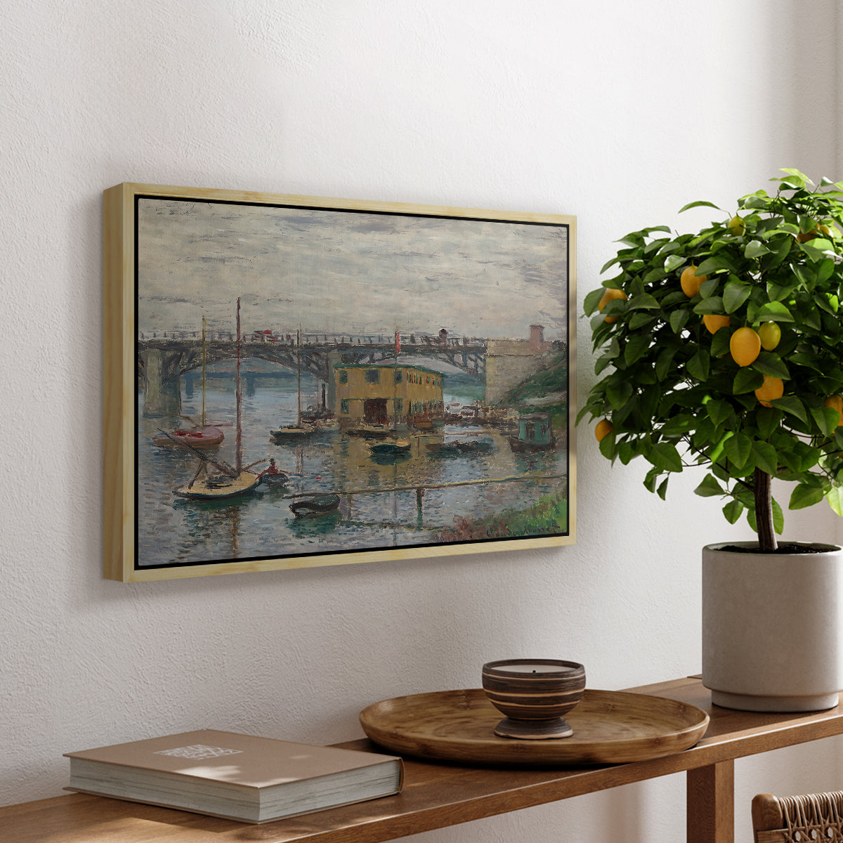 Bridge at Argenteuil on a Gray Day, c. 1876 by Claude Monet, presented in a natural wood floater framed canvas featuring a bridge crossing river under gray sky with muted reflections, displayed above a hallway console table.