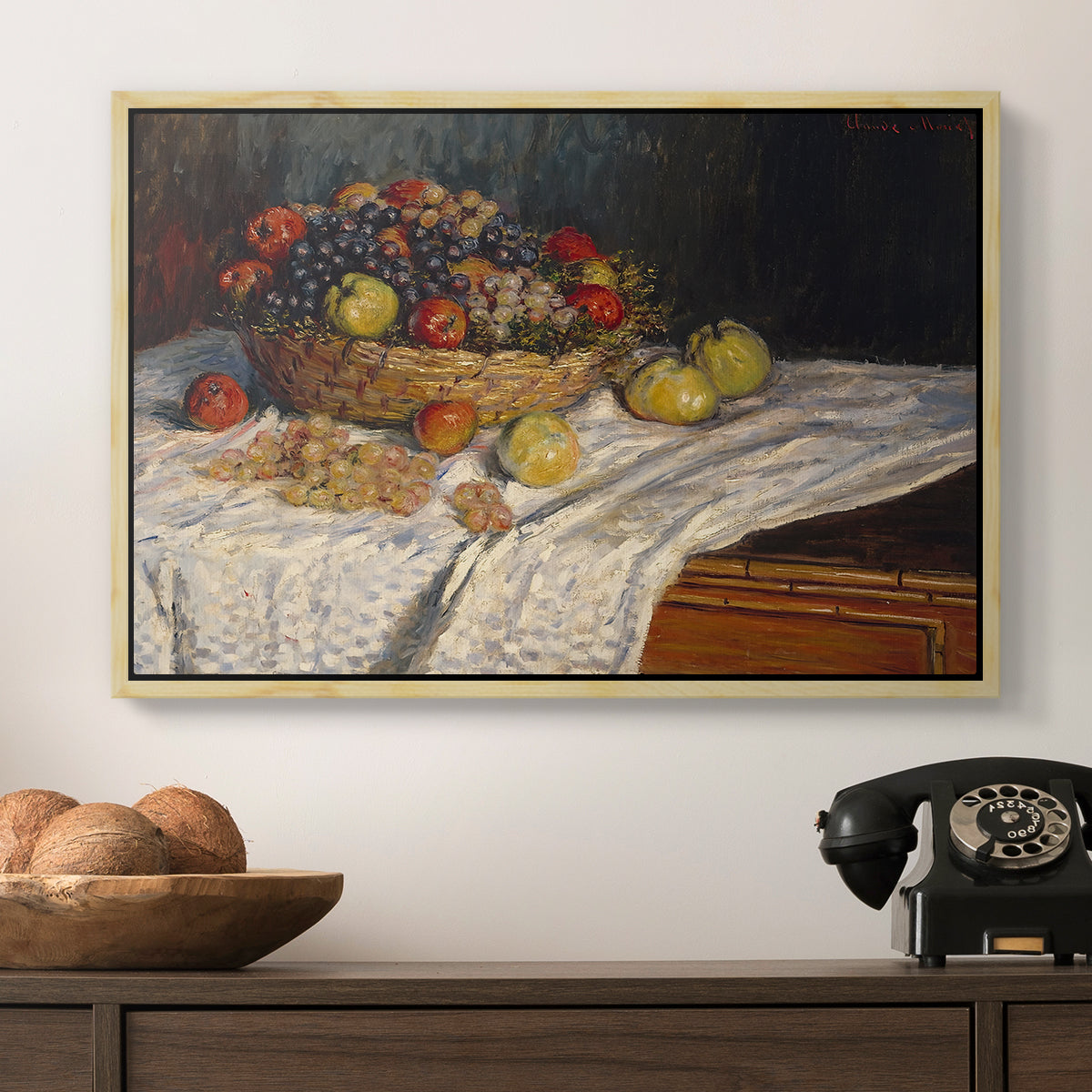 Still Life with Apples and Grapes, 1880 by Claude Monet in a natural wood floater framed canvas displayed above a console table in a hallway, featuring a tabletop composition with fruit and subtle shadows.