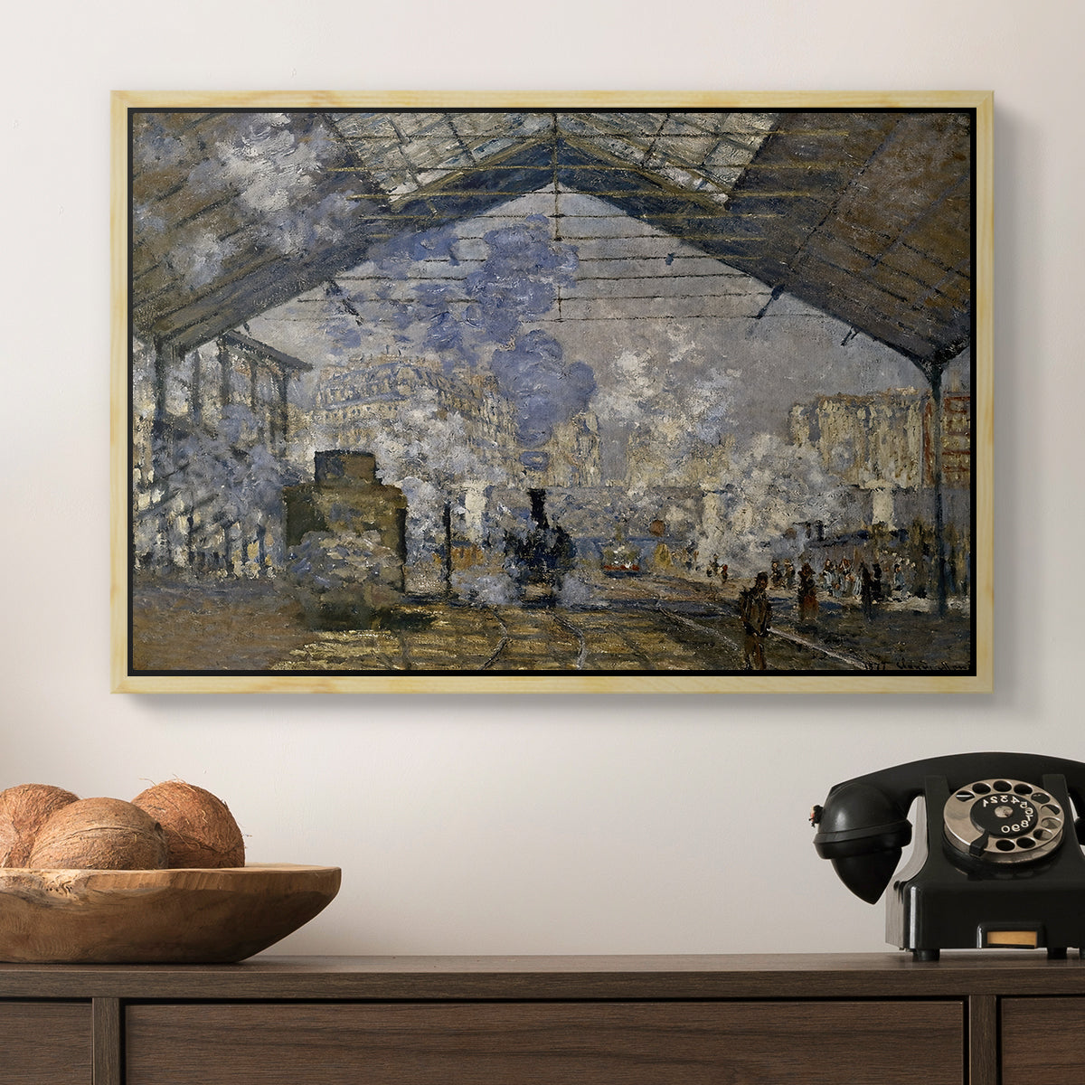 The Gare Saint-Lazare, 1877 by Claude Monet in a natural wood floater framed canvas displayed above a console table in a hallway, featuring a bustling transport hub with trains beneath glass roof.