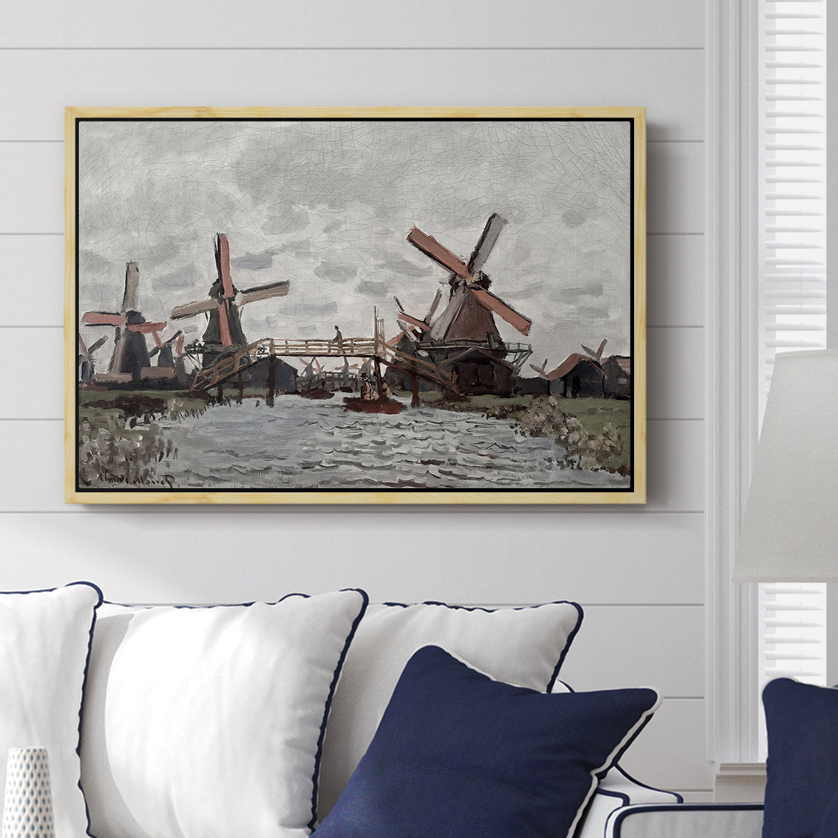 Windmills near Zaandam, 1871 by Claude Monet displayed above a sofa in a living room in a natural wood floater frame, featuring an impressionist view of Dutch windmills along riverbank.