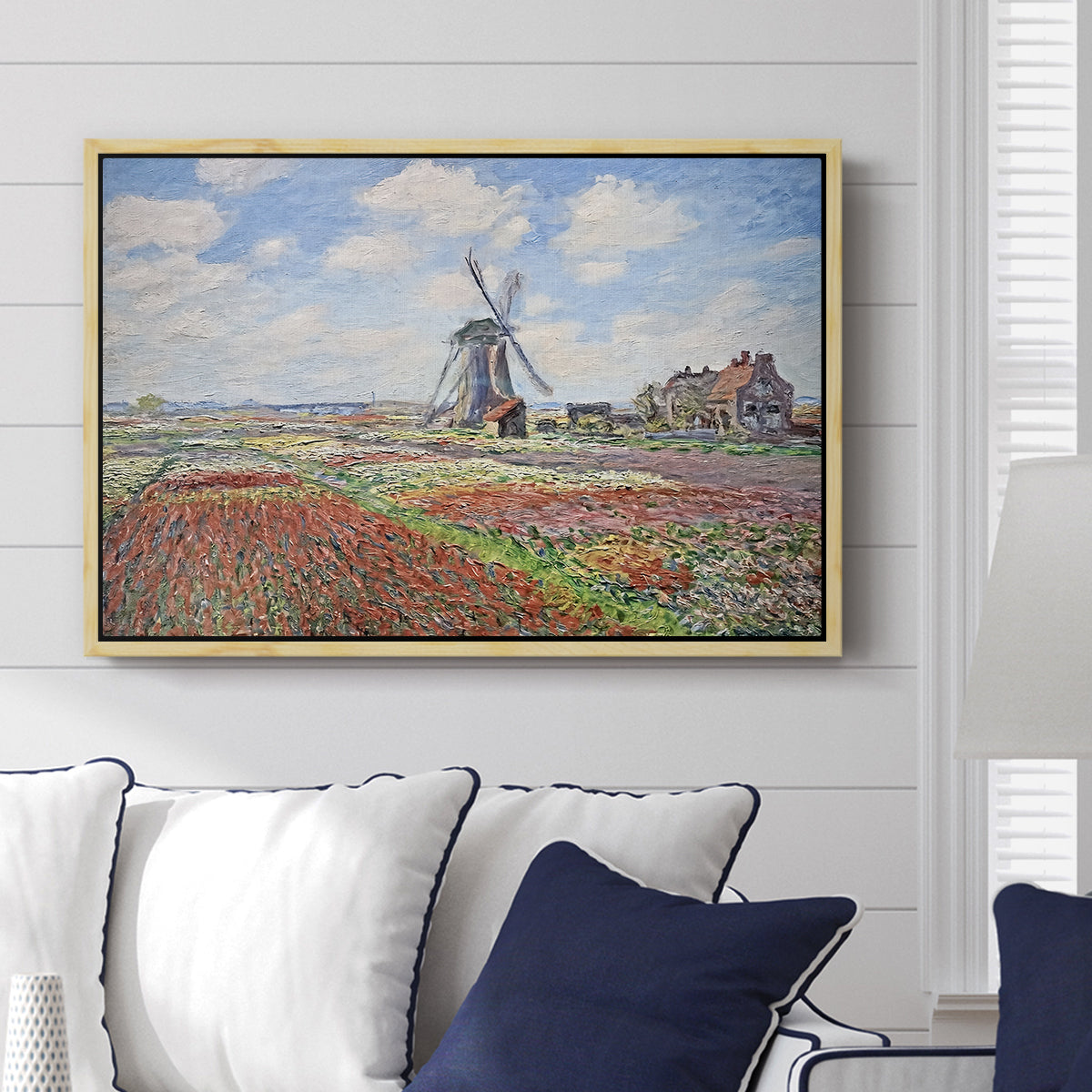 Tulip Fields with the Rijnsburg Windmill, 1886 by Claude Monet displayed above a sofa in a living room in a natural wood floater frame, featuring a vibrant agricultural landscape with flowers and windmill.
