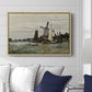 Windmill at Zaandam, 1871 by Claude Monet displayed above a sofa in a living room in a natural wood floater frame, featuring an impressionist depiction of windmill near riverbank.