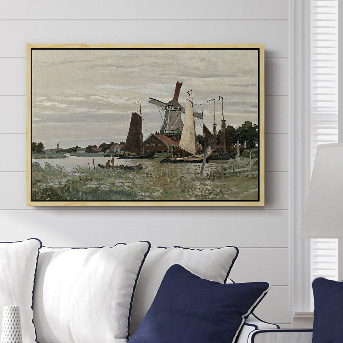 Windmill at Zaandam, 1871 by Claude Monet displayed above a sofa in a living room in a natural wood floater frame, featuring an impressionist depiction of windmill near riverbank.