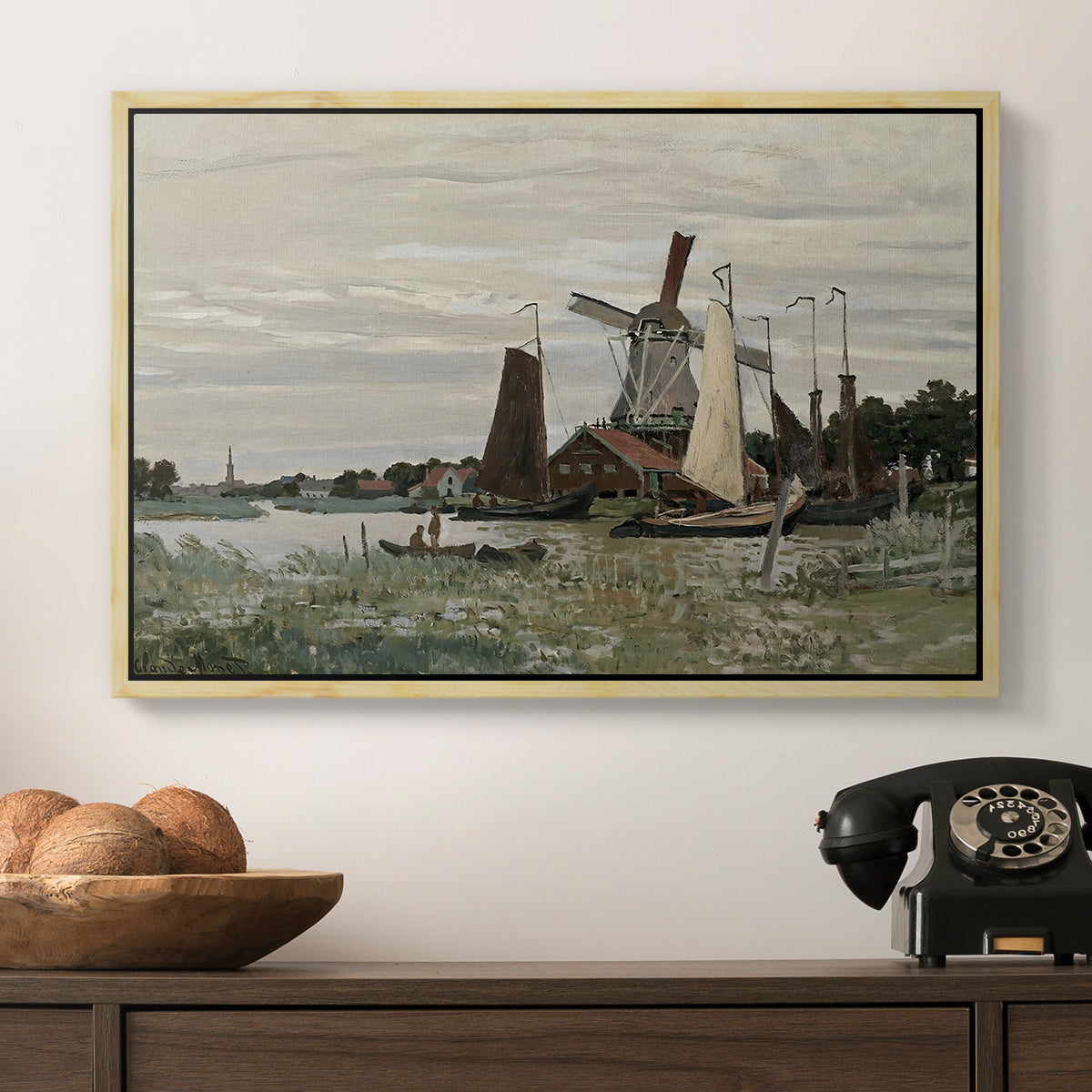 Windmill at Zaandam, 1871 by Claude Monet in a natural wood floater framed canvas displayed above a console table in a hallway, featuring a countryside structure standing against open sky.