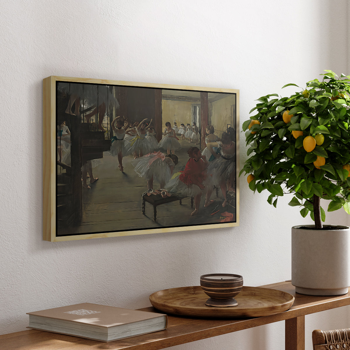The Dance Class, c. 1873 by Edgar Degas, presented in a natural wood floater framed canvas featuring ballerinas practicing in studio with instructor observing nearby, displayed above a hallway console table.