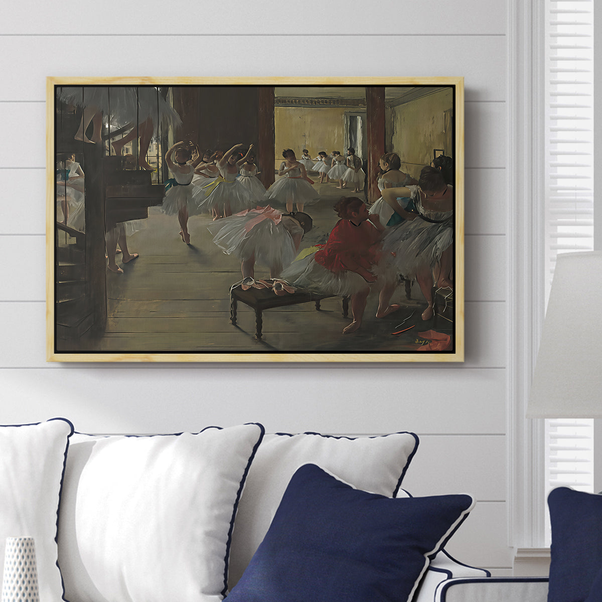 The Dance Class, c. 1873 by Edgar Degas displayed above a sofa in a living room in a natural wood floater frame, featuring a rehearsal scene with dancers stretching and posing indoors.