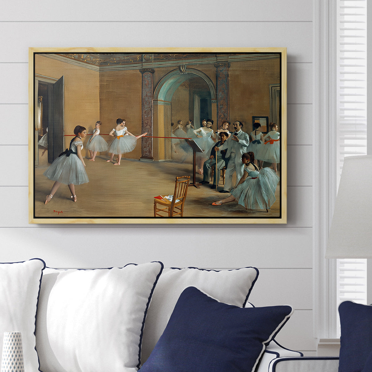 The Dance Foyer at the Opera on the Rue Le Peletier, 1872 by Edgar Degas displayed above a sofa in a living room in a natural wood floater frame, featuring an interior scene of dancers waiting and stretching in large studio.