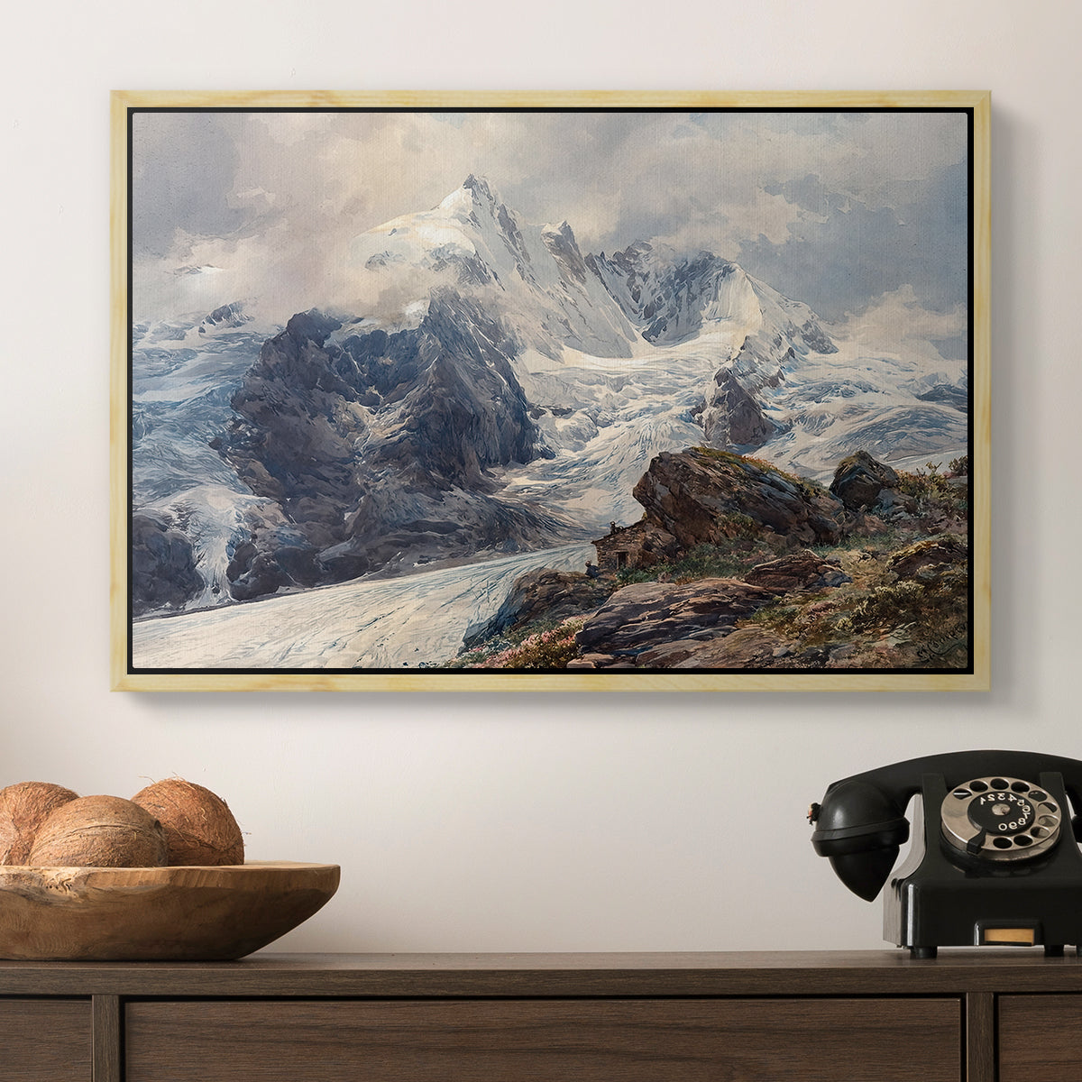 The Grossglockner, 1880 by Edward Theodore Compton in a natural wood floater framed canvas displayed above a console table in a hallway, featuring an alpine peak dominating surrounding terrain.