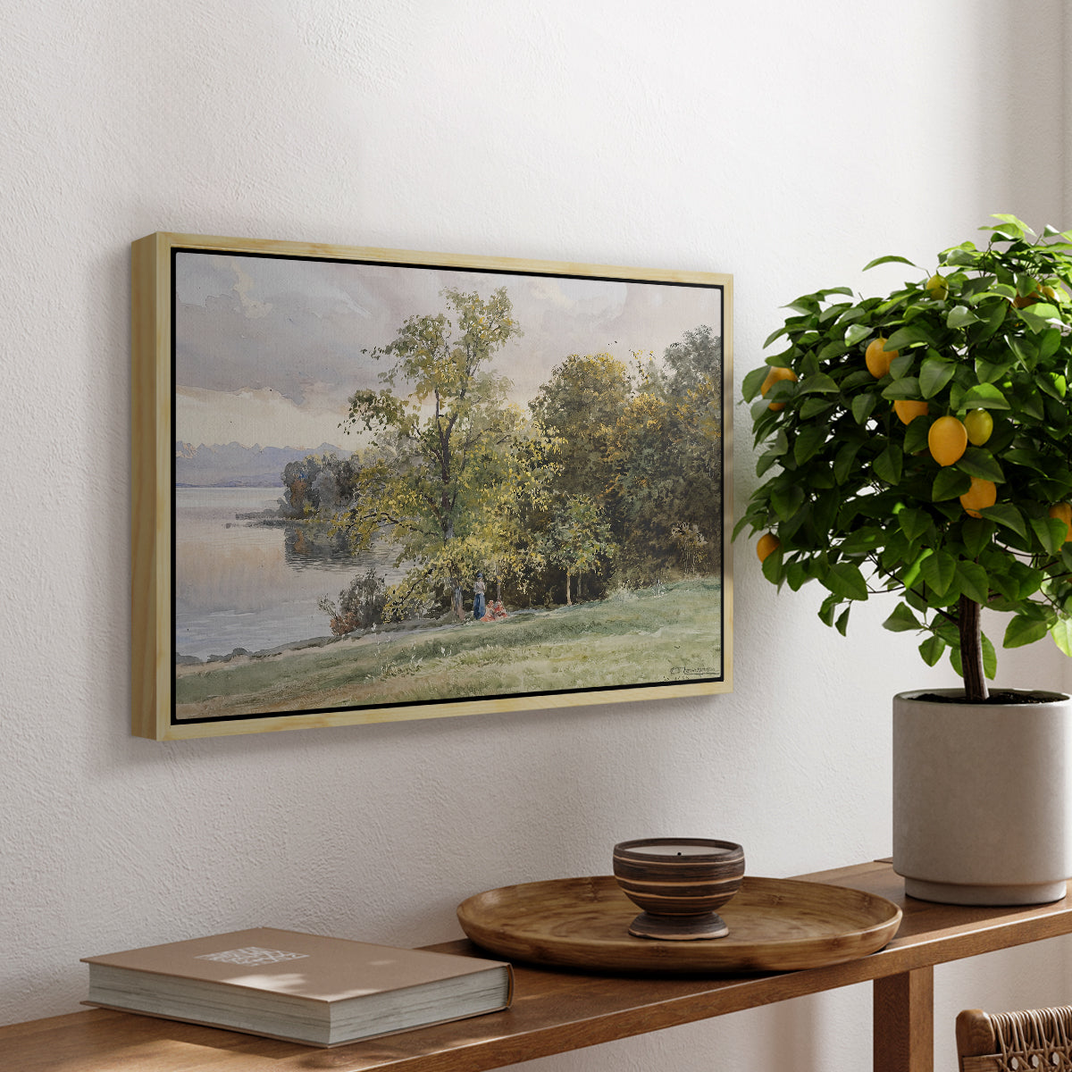Landscape at Lake Starnberg, 1890 by Edward Theodore Compton, presented in a natural wood floater framed canvas featuring a lakeside landscape with calm water and trees along shoreline, displayed above a hallway console table.