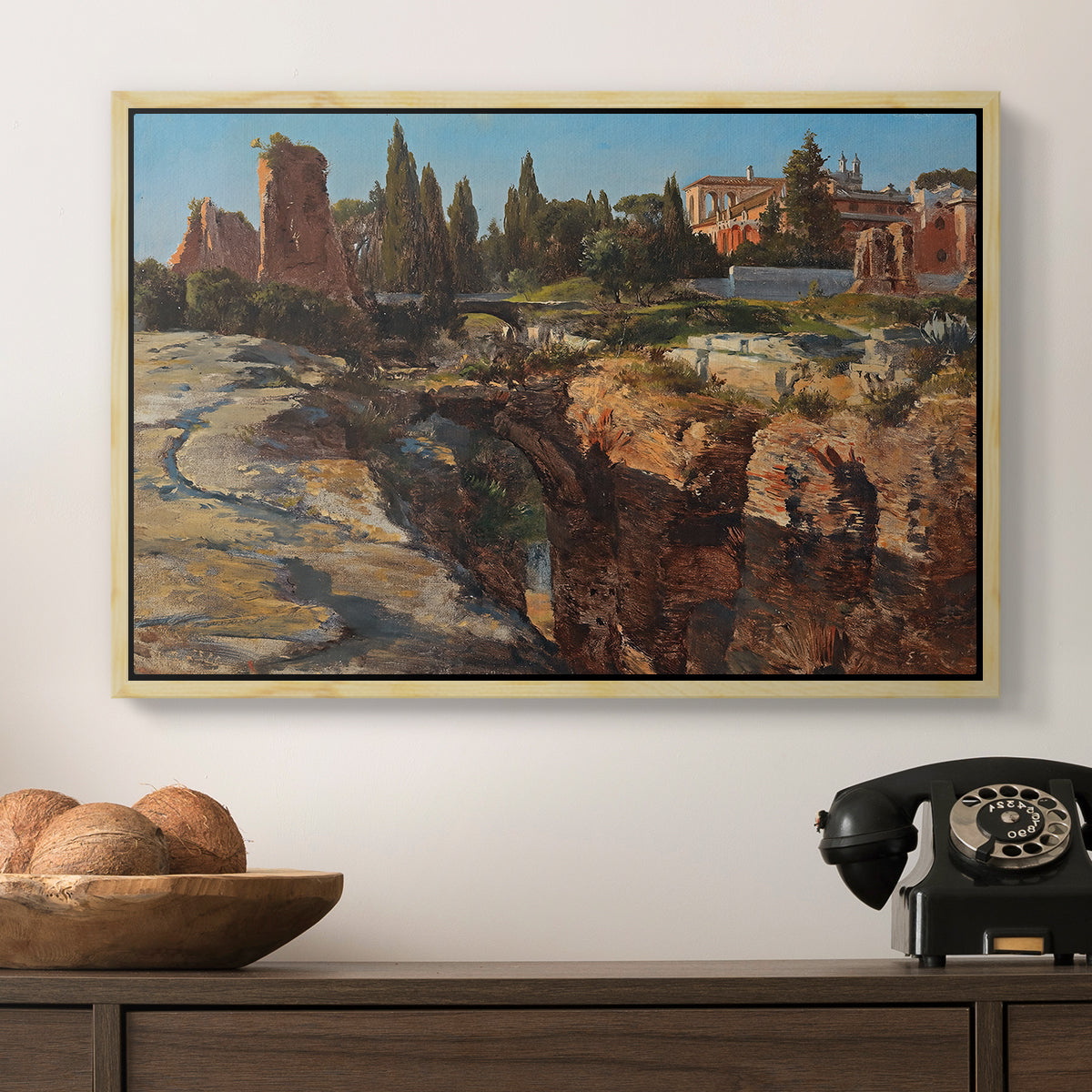 Palatine in Rome, c. 1921 by Edward Theodore Compton in a natural wood floater framed canvas displayed above a console table in a hallway, featuring a detailed depiction of historic Roman architecture.