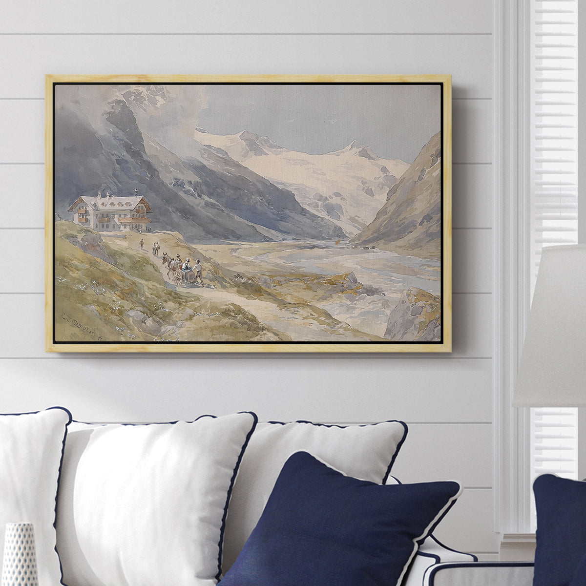 Shepherds (Pasterze), c. 1921 by Edward Theodore Compton displayed above a sofa in a living room in a natural wood floater frame, featuring a pastoral mountain scene with figures tending livestock.