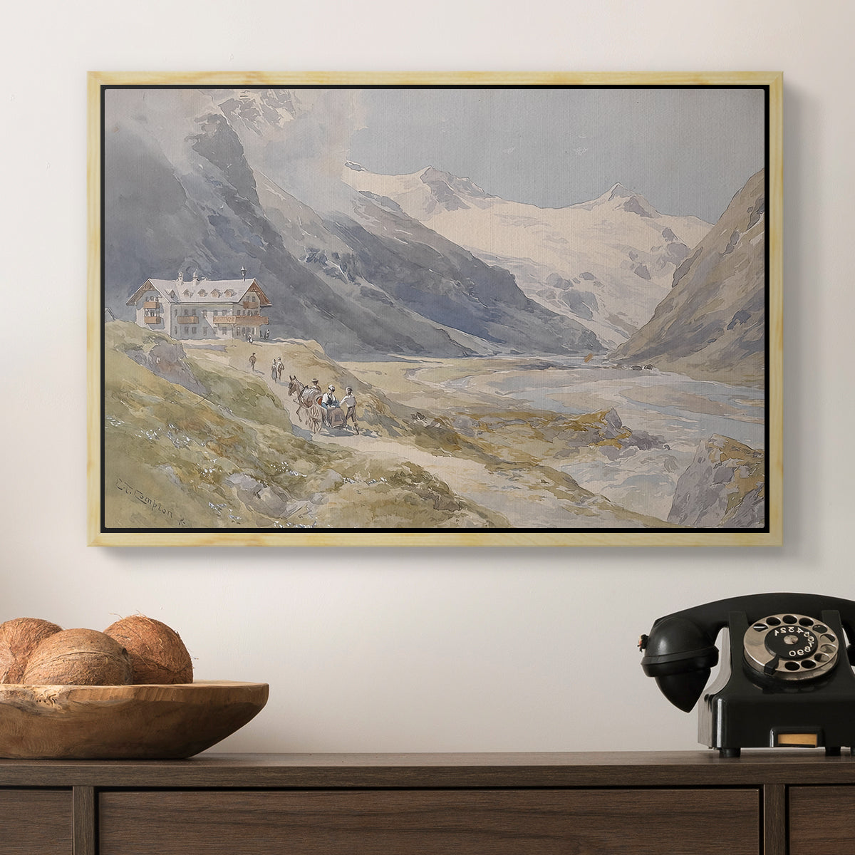 Shepherds (Pasterze), c. 1921 by Edward Theodore Compton in a natural wood floater framed canvas displayed above a console table in a hallway, featuring a natural landscape with human presence among mountains.