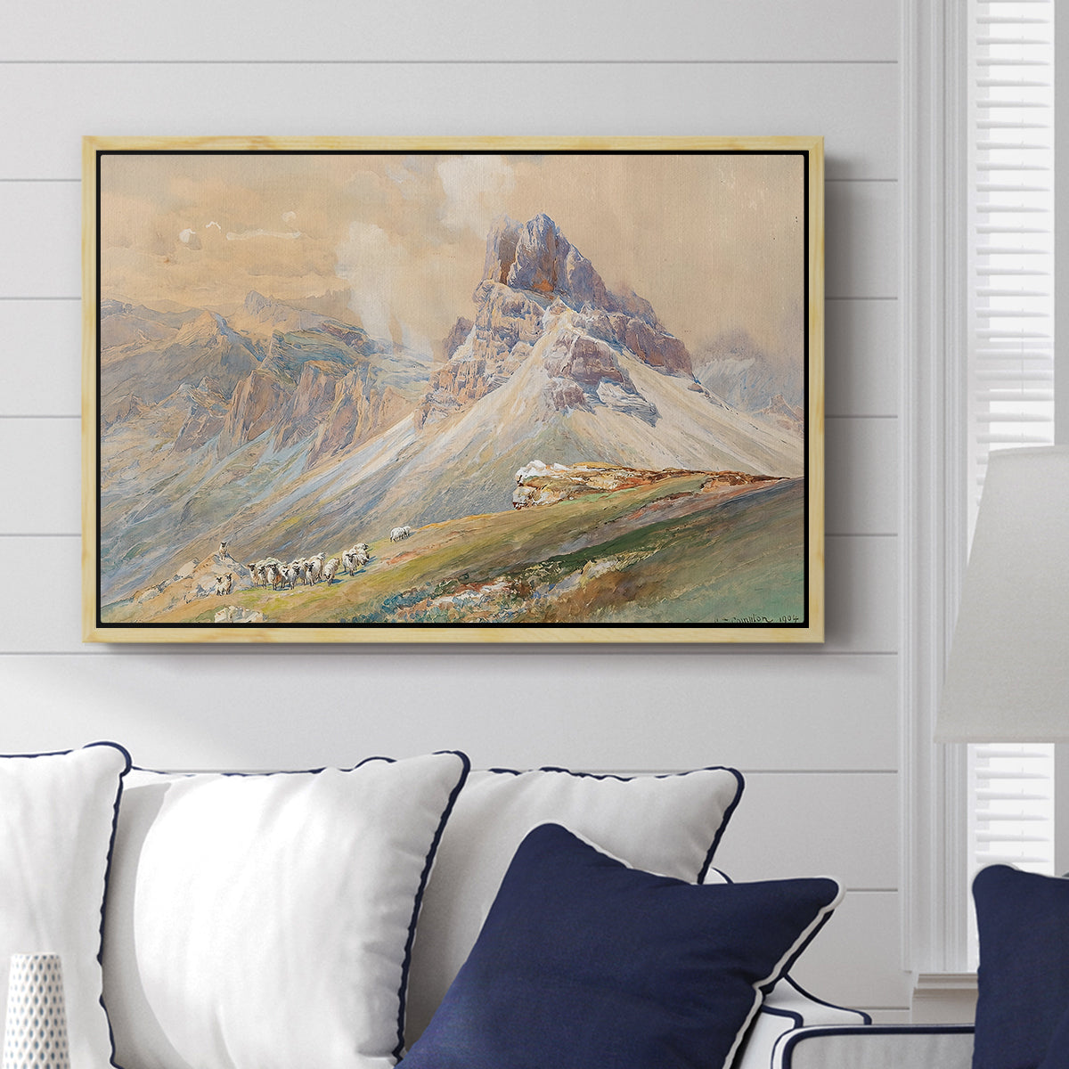 From the Dolomites, 1904 by Edward Theodore Compton displayed above a sofa in a living room in a natural wood floater frame, featuring an alpine scene with jagged rock formations and distant mountains.