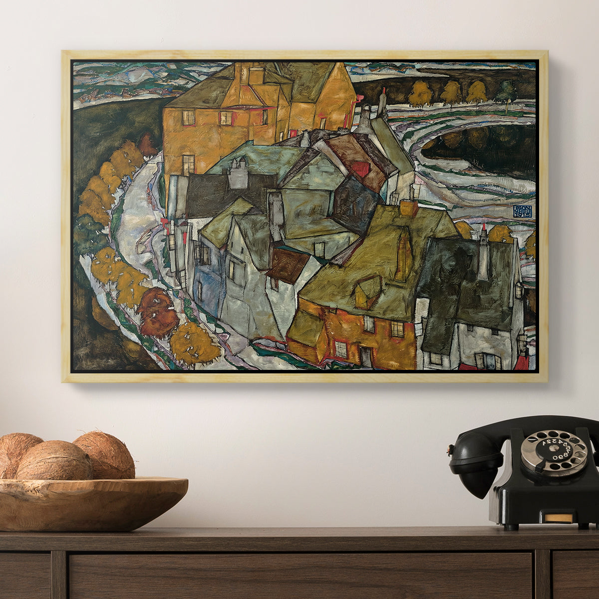Crescent of Houses II (Island Town), 1915 by Egon Schiele in a natural wood floater framed canvas displayed above a console table in a hallway, featuring an architectural scene with houses arranged in curved composition.