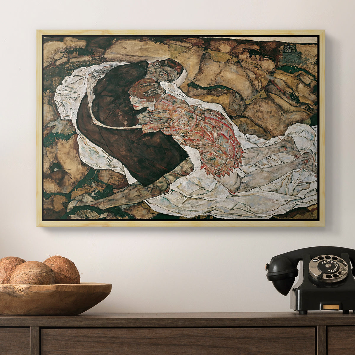 Death and the Maiden, 1915 by Egon Schiele in a natural wood floater framed canvas displayed above a console table in a hallway, featuring an intense composition exploring life and death through figures.