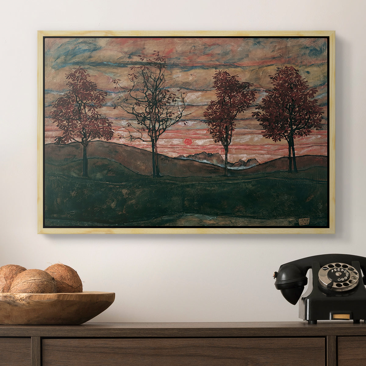 Four Trees, 1917 by Egon Schiele in a natural wood floater framed canvas displayed above a console table in a hallway, featuring an expressionist landscape featuring isolated trees in field.