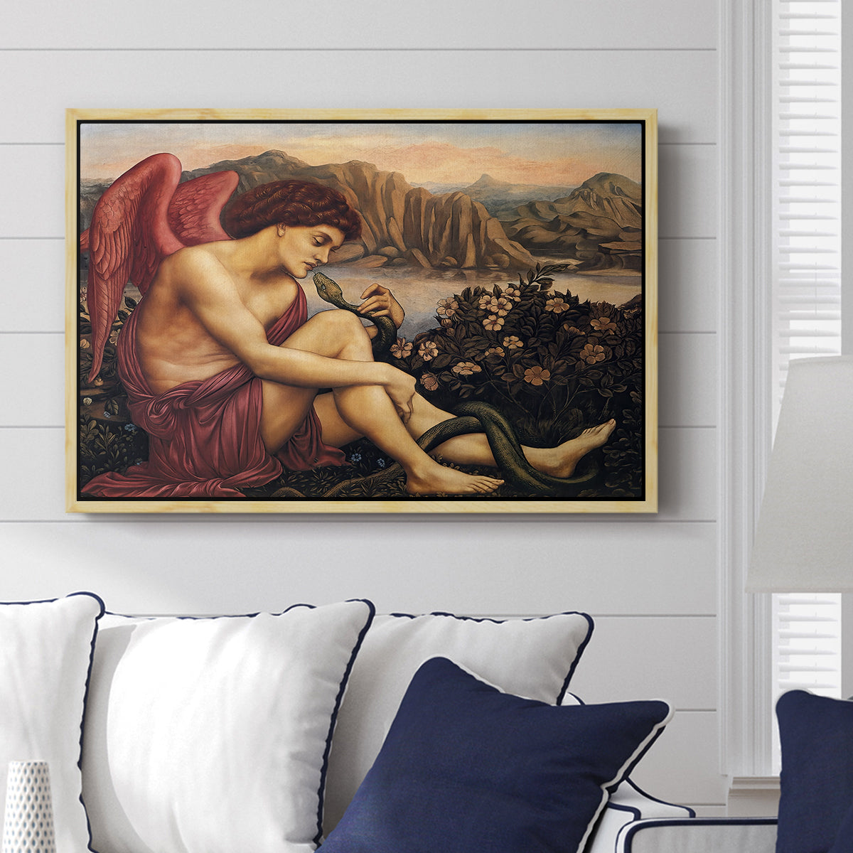 The Angel with the Serpent, c. 1870-1875 by Evelyn De Morgan displayed above a sofa in a living room in a natural wood floater frame, featuring a winged figure standing over serpent in allegorical composition.