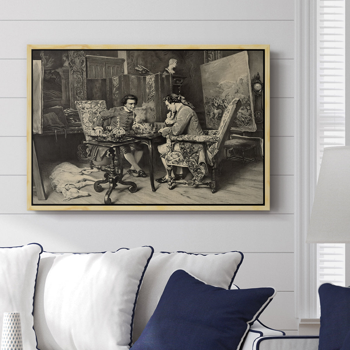 The Chess Players, 1858 by Ernest Meissonier displayed above a sofa in a living room in a natural wood floater frame, featuring a realistic scene of figures concentrating on chess game indoors.