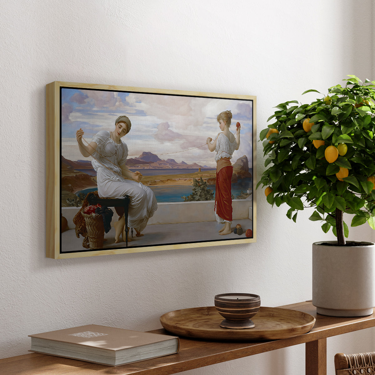 Winding the Skein, c. 1878 by Frederic Leighton, presented in a natural wood floater framed canvas featuring a woman holding thread while another figure helps wind yarn in classical setting, displayed above a hallway console table.