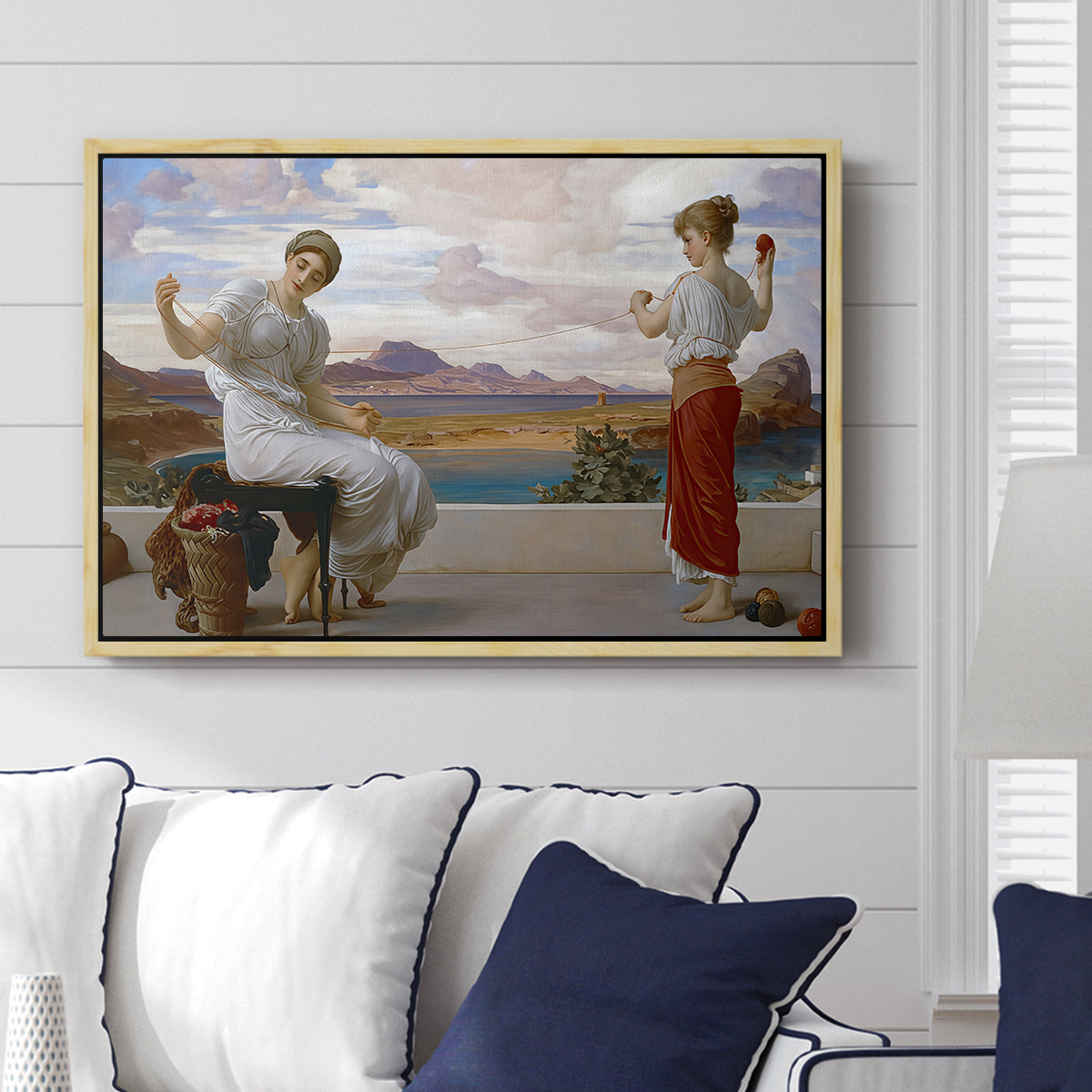 Winding the Skein, c. 1878 by Frederic Leighton displayed above a sofa in a living room in a natural wood floater frame, featuring two women engaged in textile work with draped garments.
