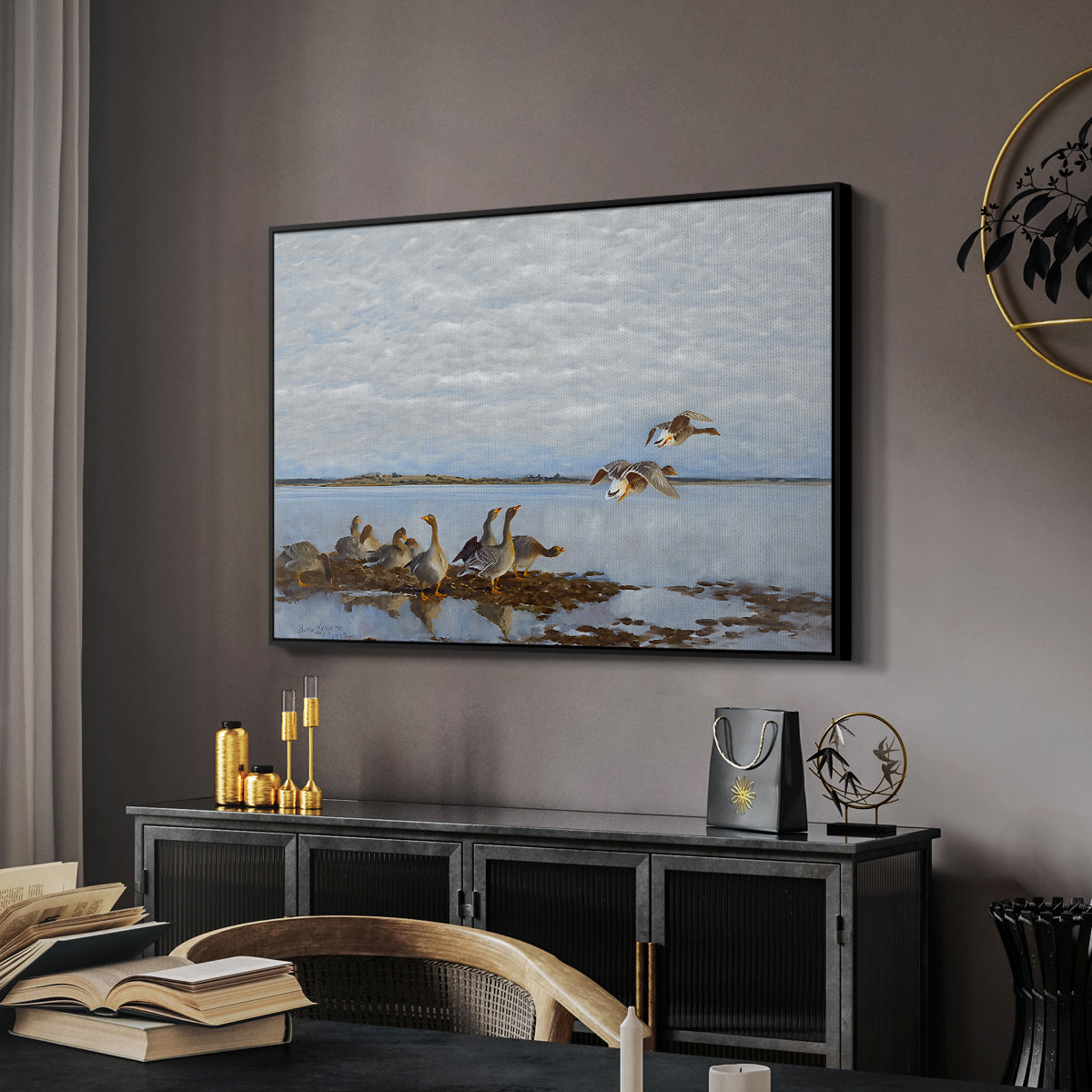 Greylag Geese (Grågäss), 1922 by Bruno Liljefors in a black floater framed canvas featuring a realistic wildlife scene of geese in calm outdoor environment, displayed above a desk in a dark home office interior.