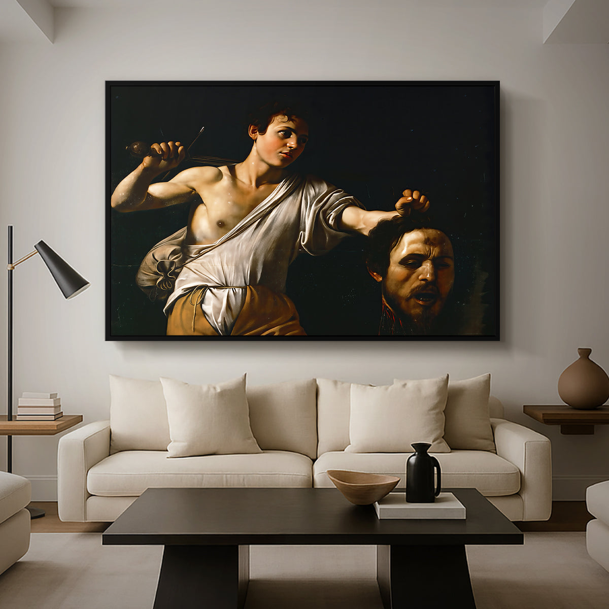 David with the Head of Goliath (Vienna Version), c. 1607 by Caravaggio as a black floater framed canvas featuring a young David holding the severed head of Goliath against a dark background, displayed above a sofa in a modern living room.