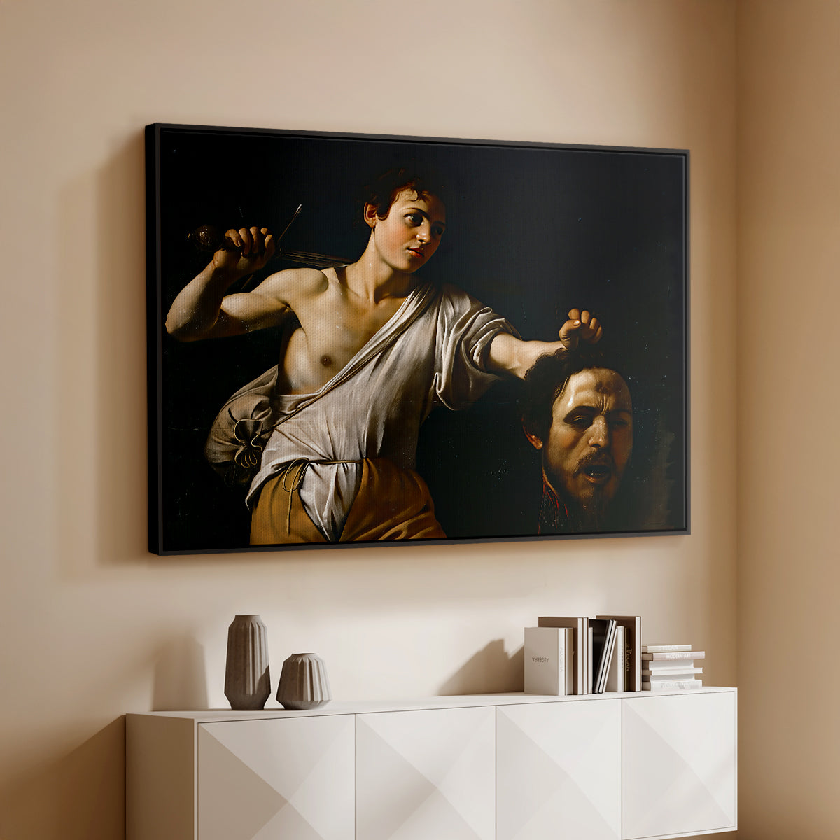 Black floater framed canvas of David with the Head of Goliath (Vienna Version), c. 1607 by Caravaggio, featuring a biblical scene of David gripping Goliath's head with dramatic lighting above a console cabinet in a minimalist entryway.