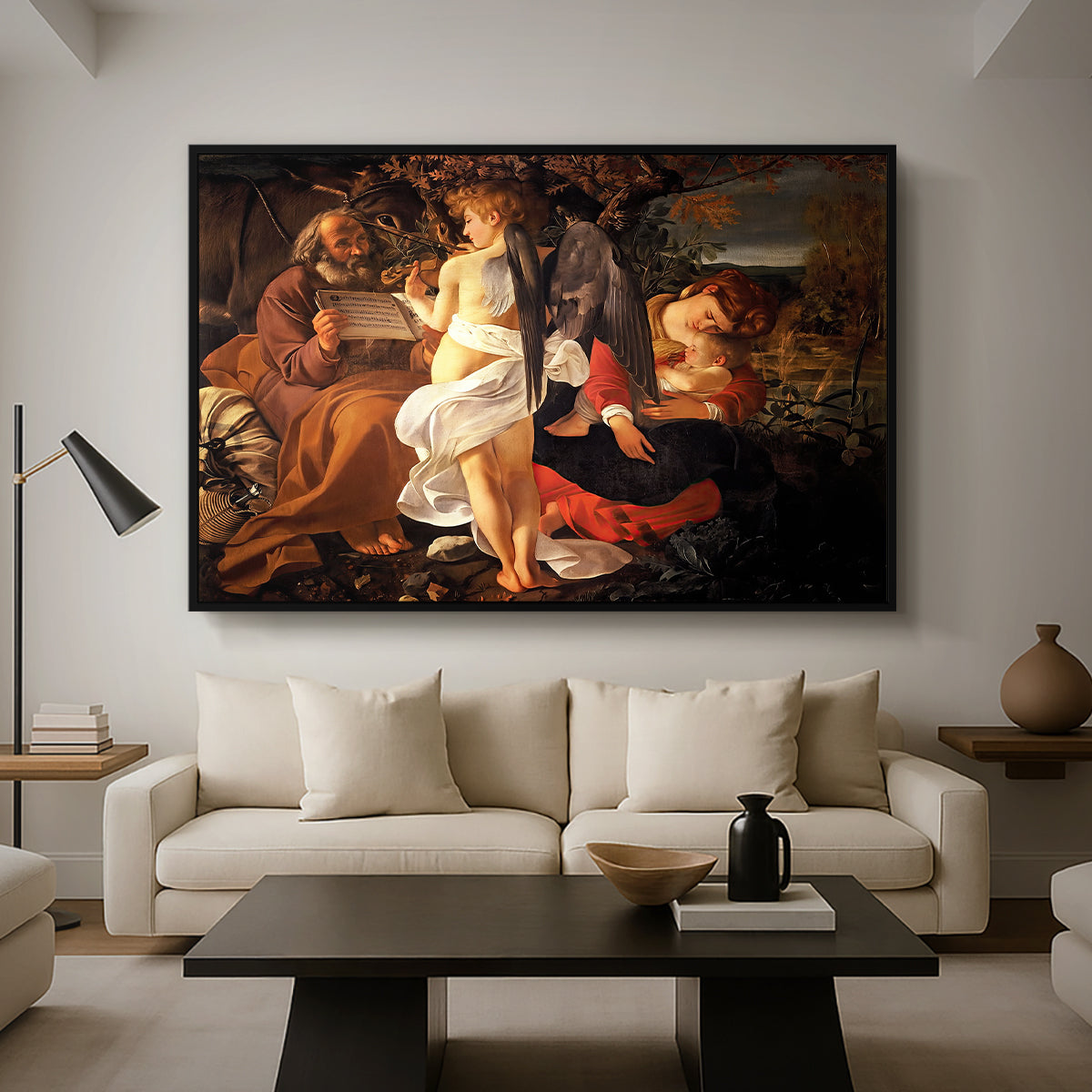 Rest on the Flight into Egypt, c. 1597 by Caravaggio as a black floater framed canvas featuring the Holy Family resting in landscape with angel playing violin, displayed above a sofa in a modern living room.